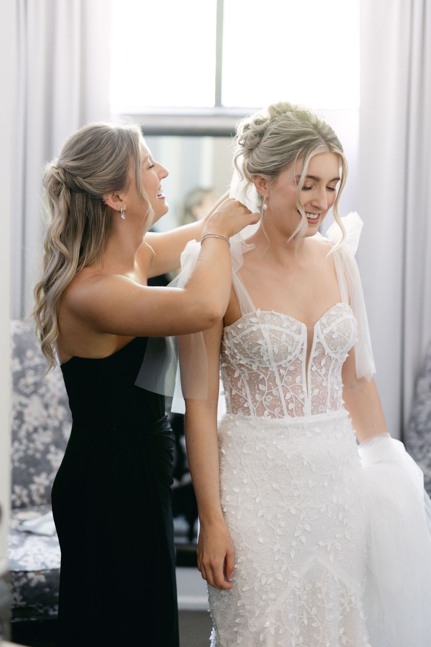 Wedding dress being adjusted in bright white room with natural lighting.