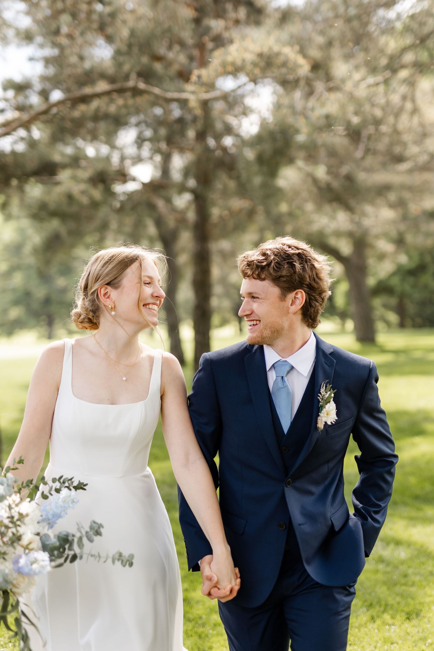 Happy couple holding hands while walking through sun-dappled garden.