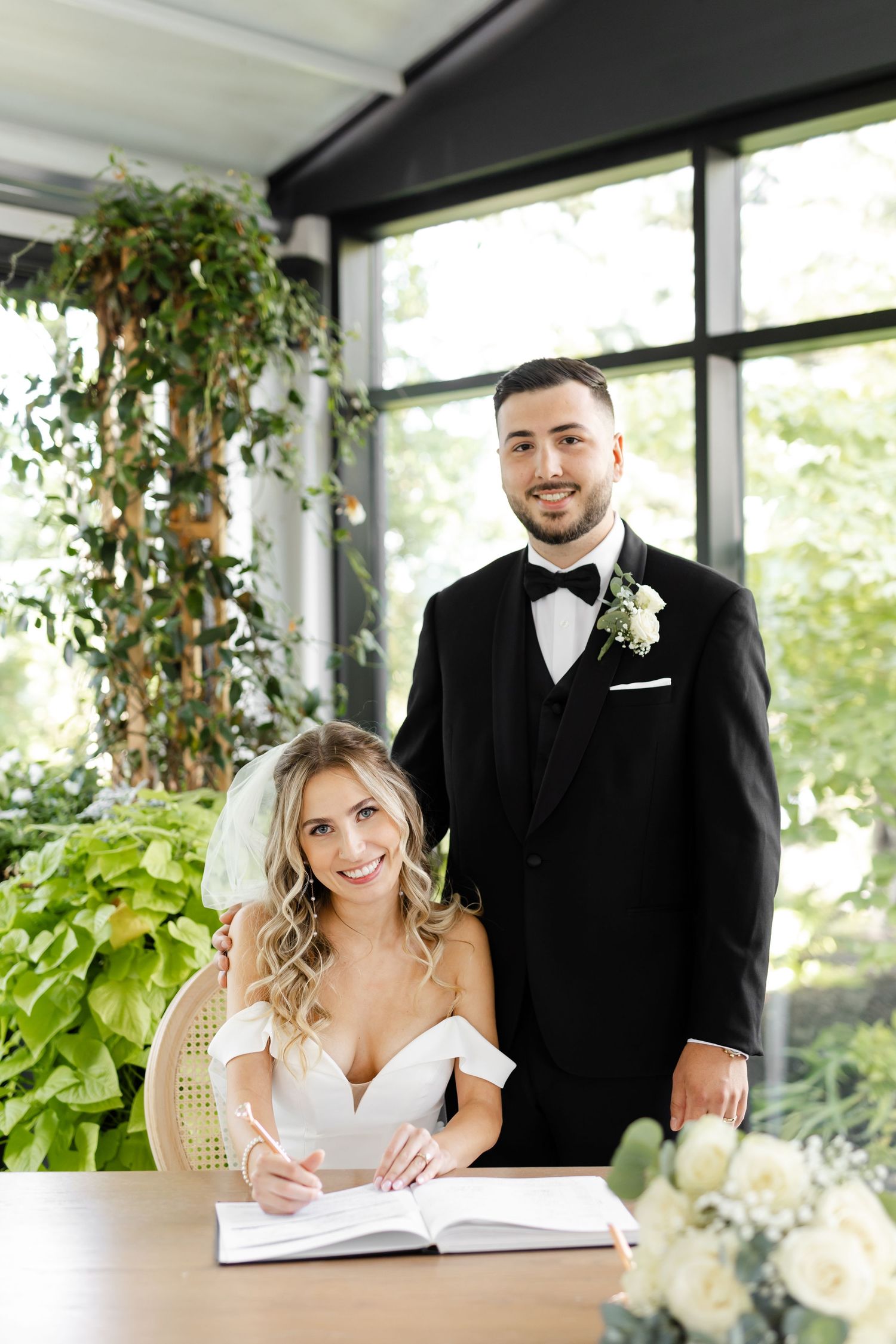 Couple signing marriage documents at decorated indoor ceremony space.