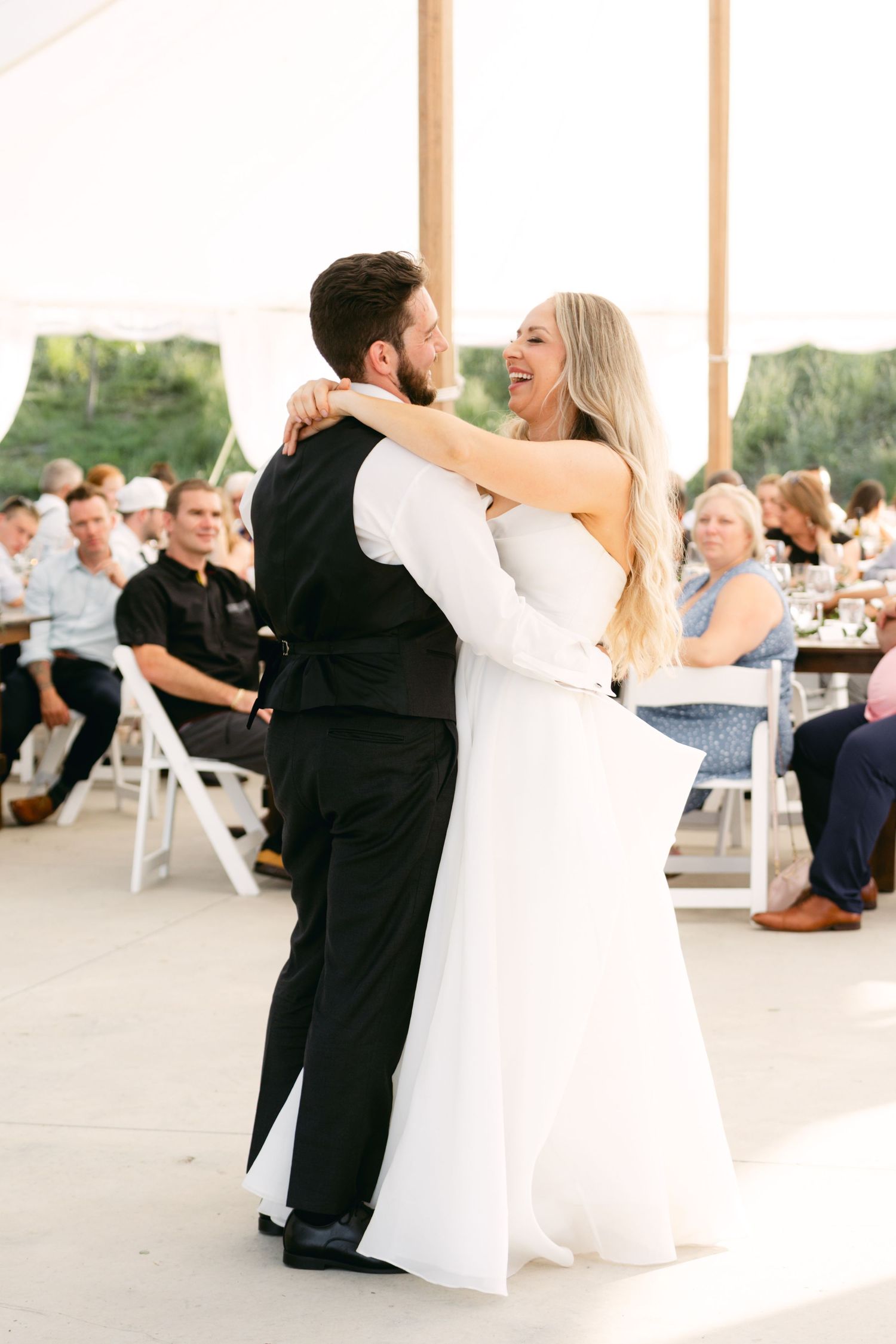 Couples dancing together during a joyful wedding reception under a white tent.