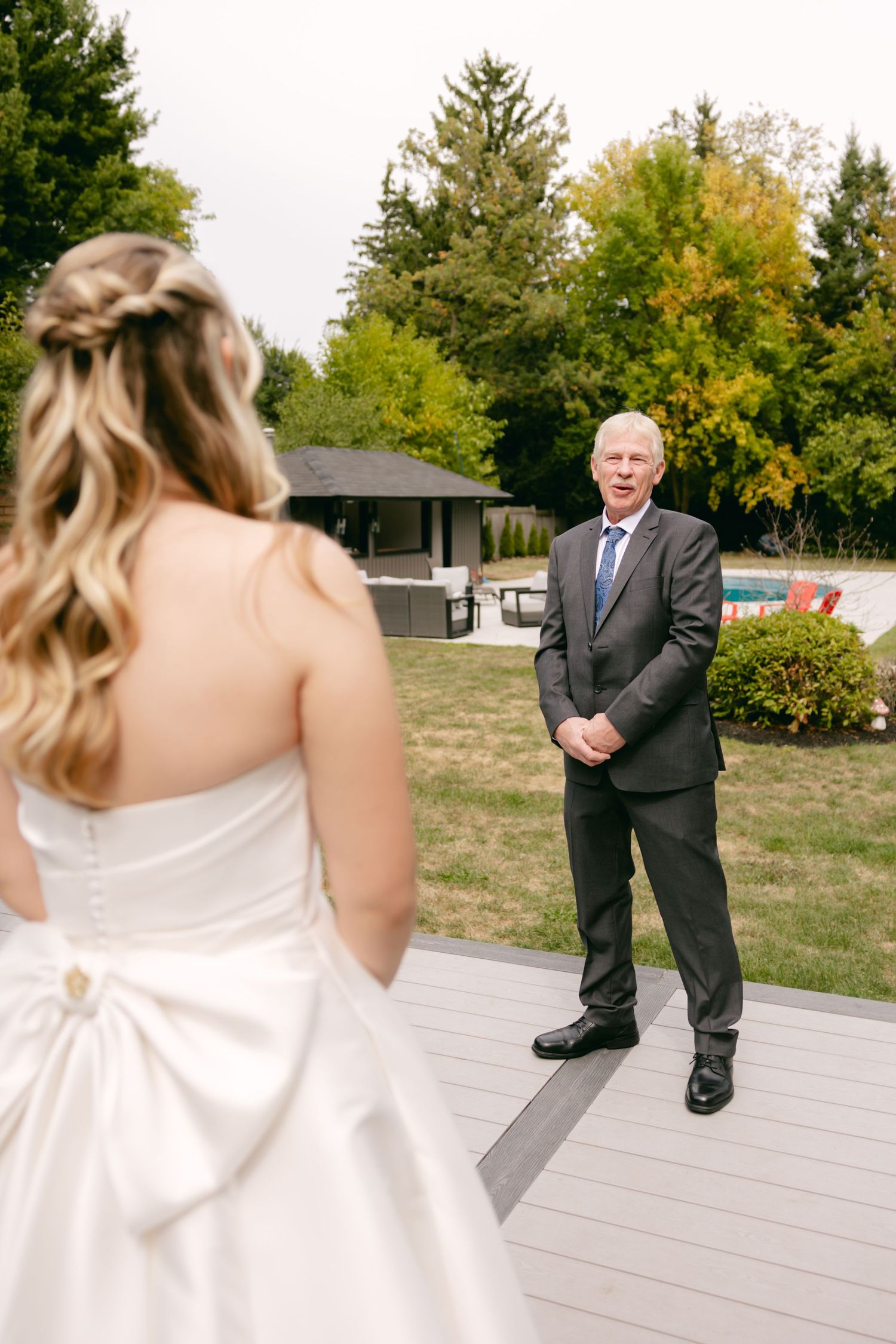 First look moment captured between bride and suited figure on outdoor wooden deck.