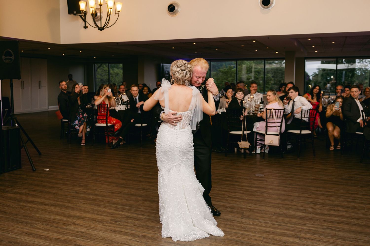 Joyful celebration on the dance floor with guests dancing under ornate chandeliers at a wedding reception.