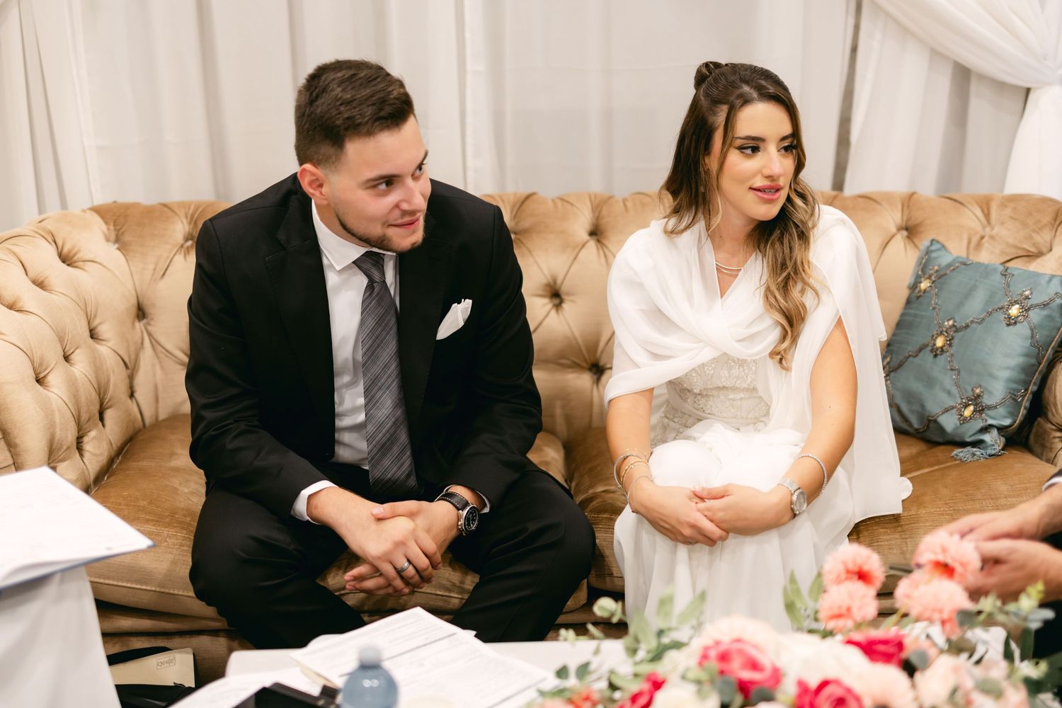 Couple seated on a beige tufted couch during a formal event.