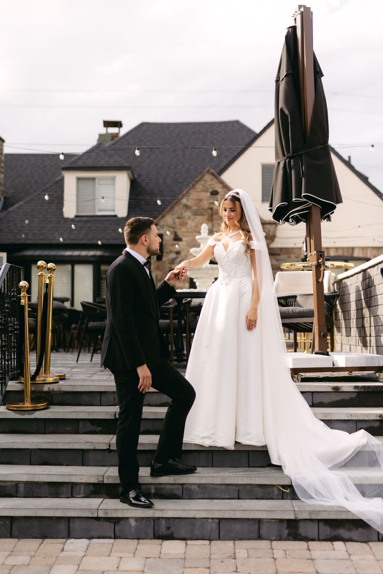 Wedding couple shares tender moment on outdoor patio with dramatic veil movement.