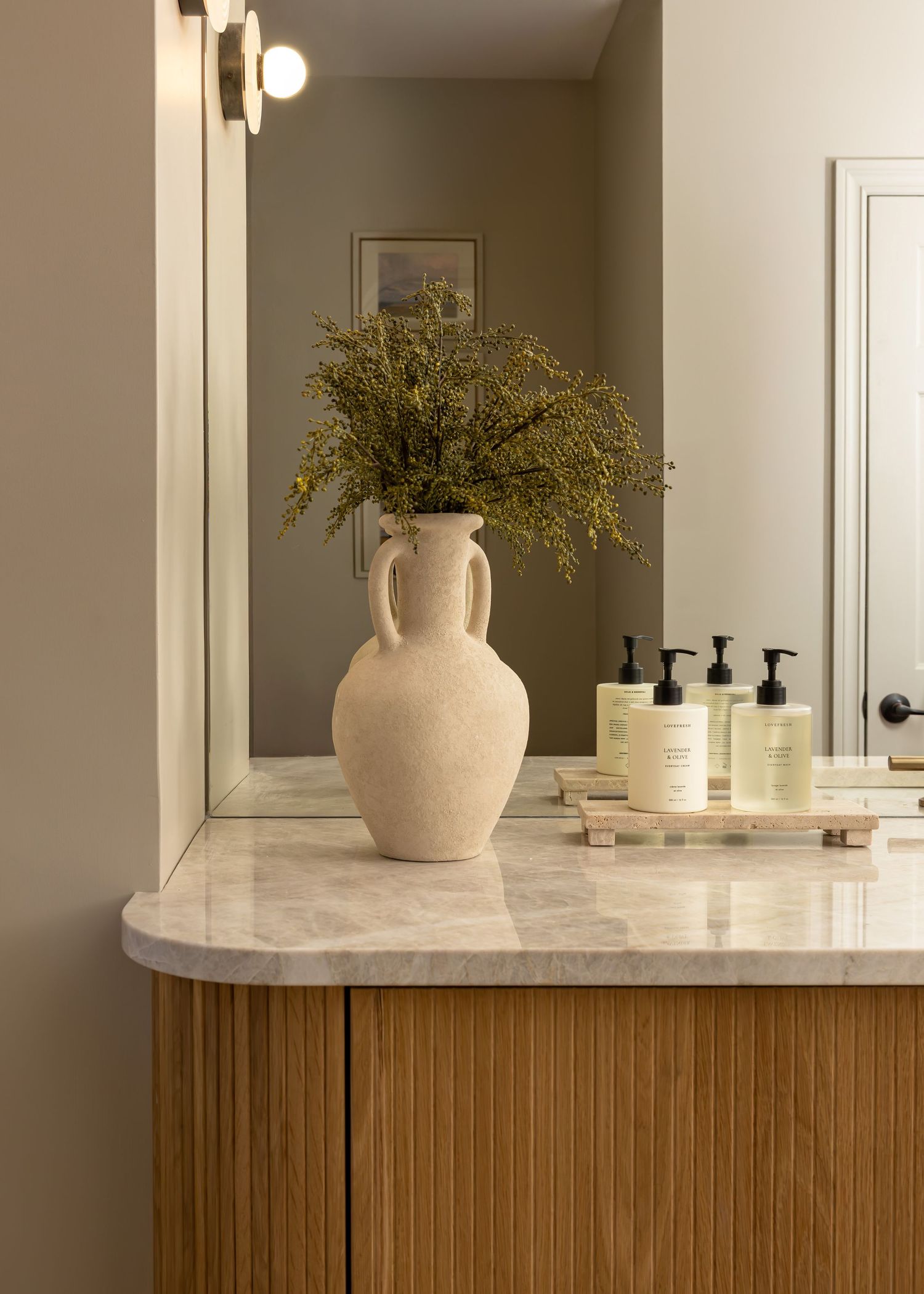 Elegant bathroom counter with light wood cabinetry and white ceramic vessel featuring fresh greenery.