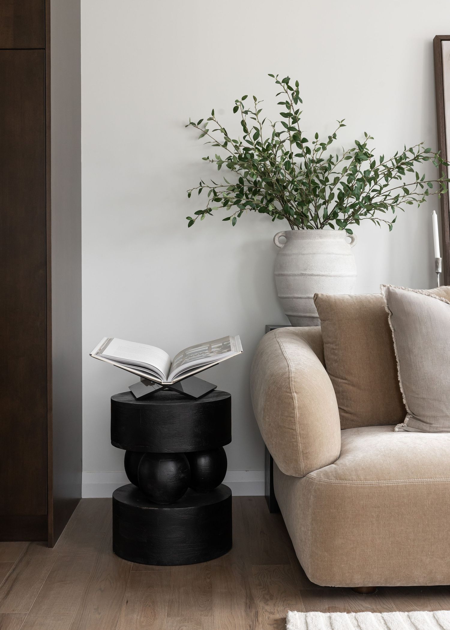 Black sculptural side table with open book display next to beige sofa and potted greenery.