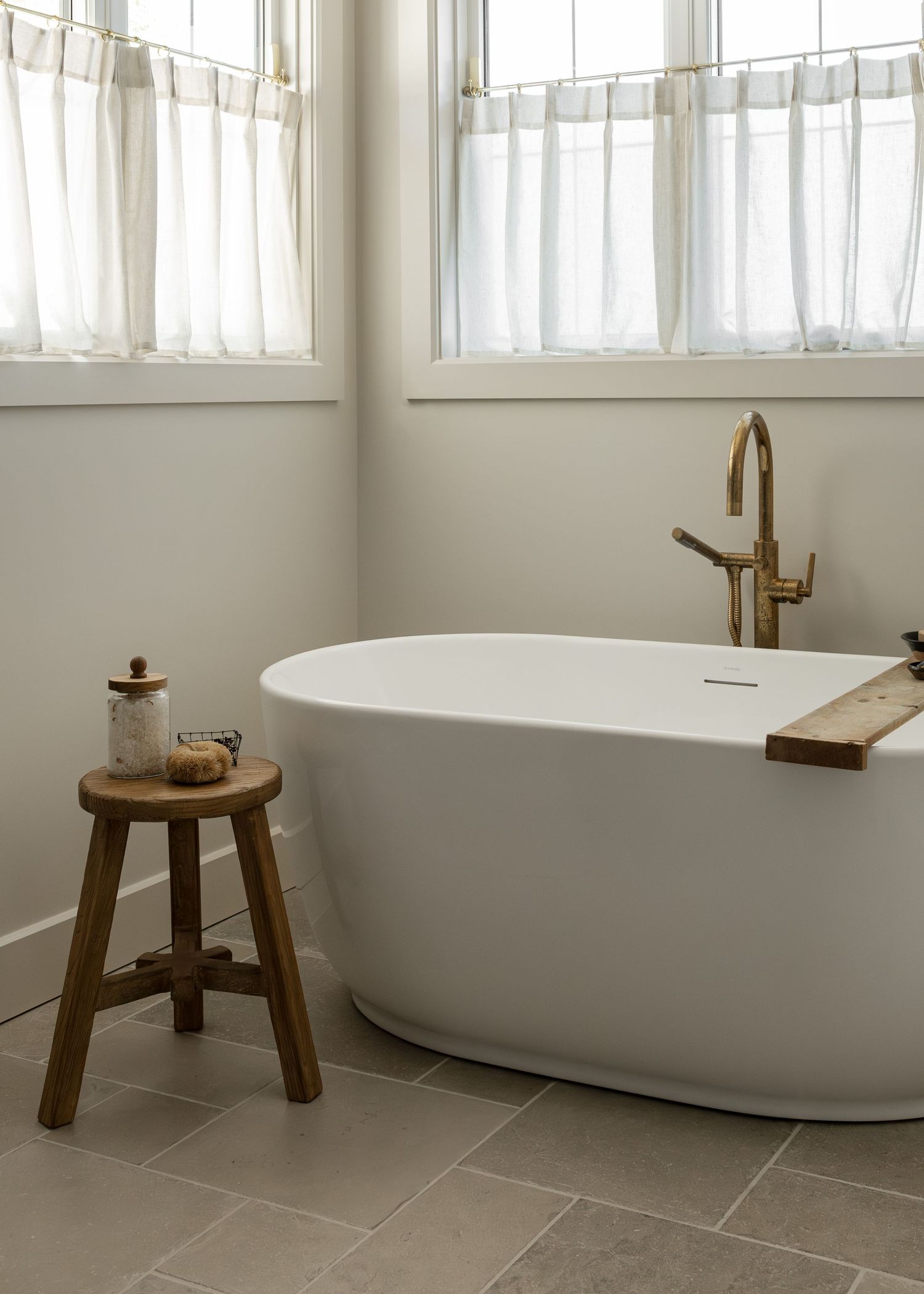 Minimalist bathroom featuring a modern oval tub, wooden stool, and sheer curtained windows.