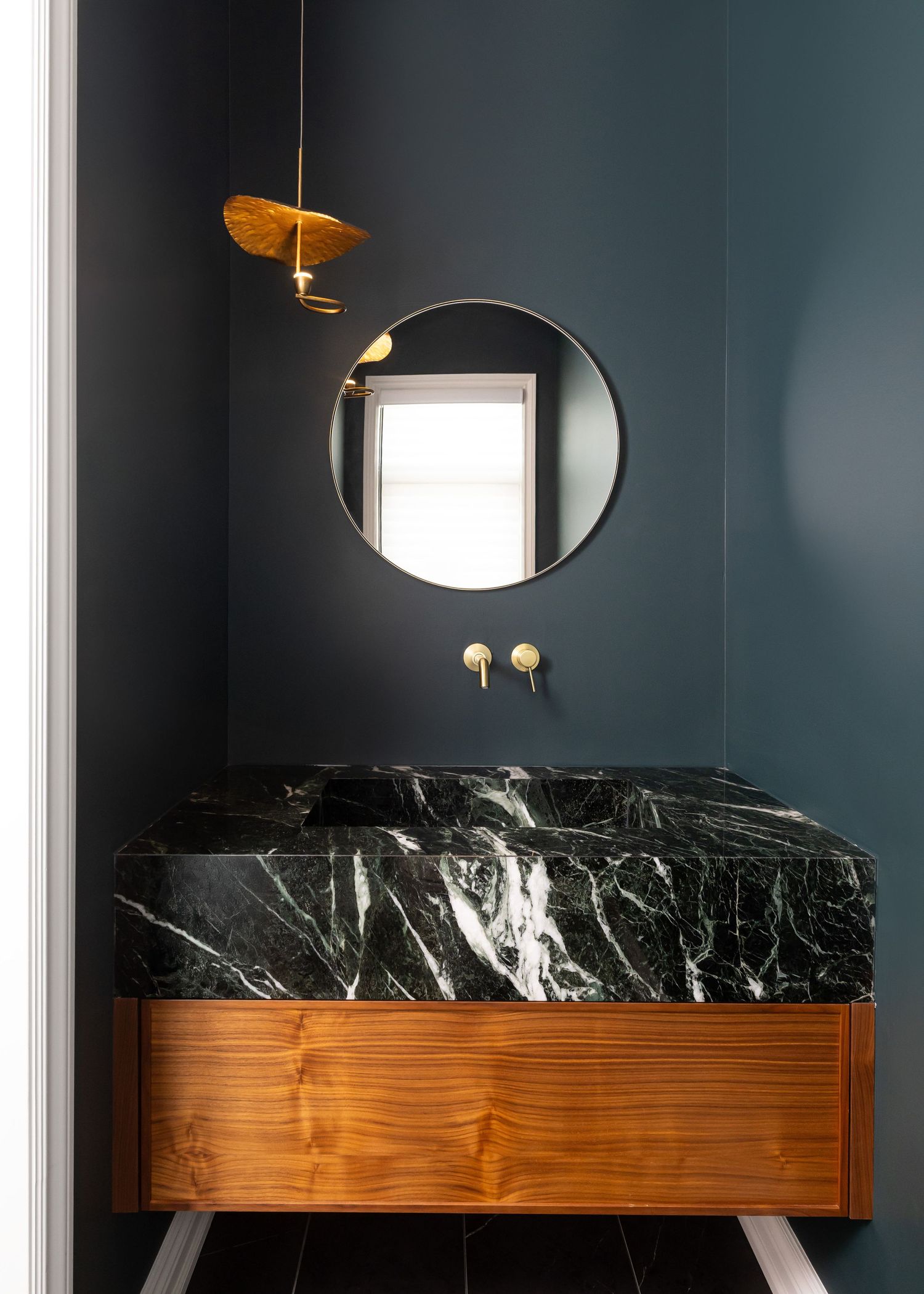 Bathroom vanity with dark marble countertop, wooden base, and round mirror.