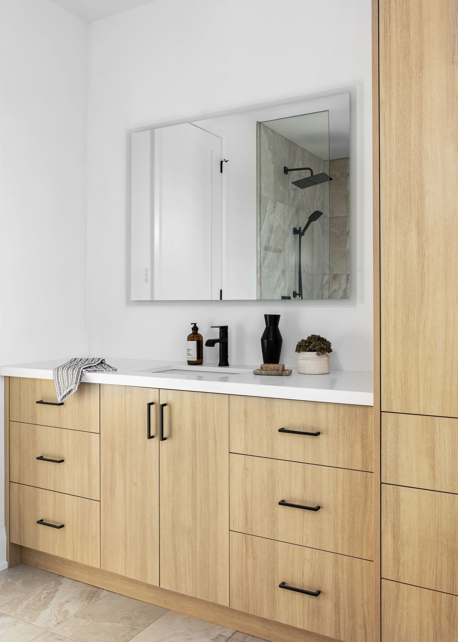 Custom built-in wood cabinetry with black handles spans the length of a bright, modern bathroom.