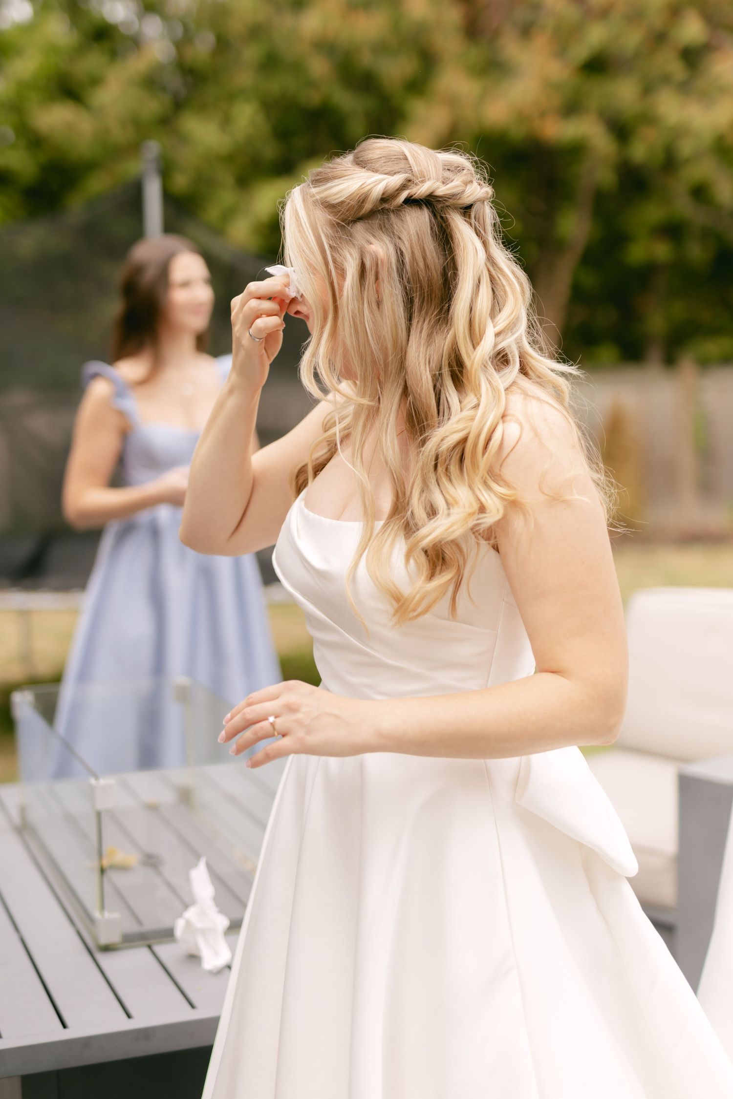 A bride in a white ballgown dances on a deck with someone in a blue dress visible in the background.