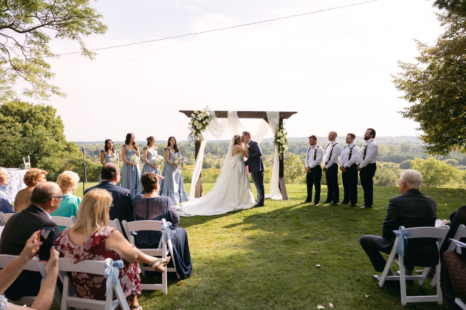 Panoramic view of outdoor wedding ceremony setup with white chairs and floral decorations.