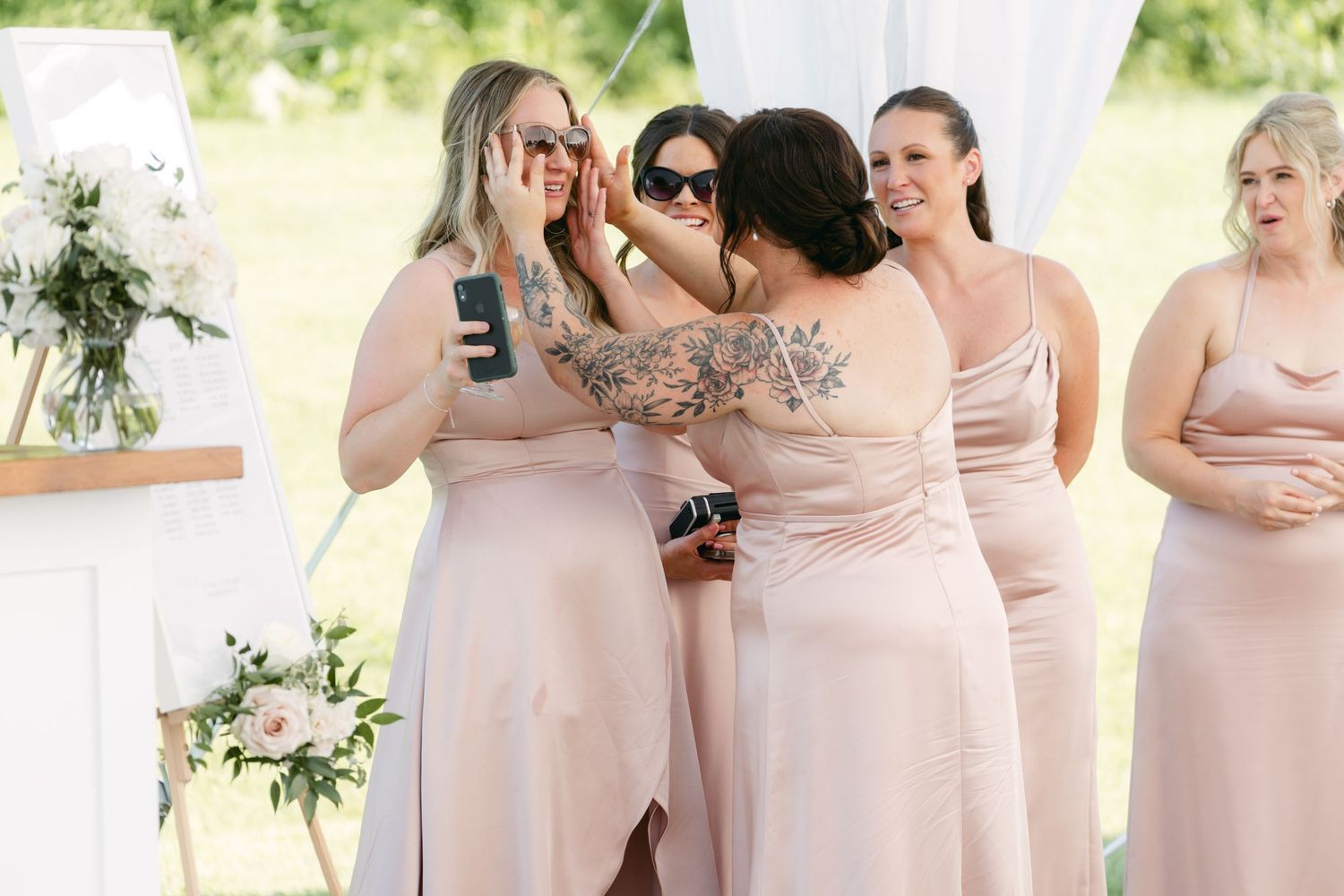 Wedding party members in soft pink dresses gather during outdoor celebration.