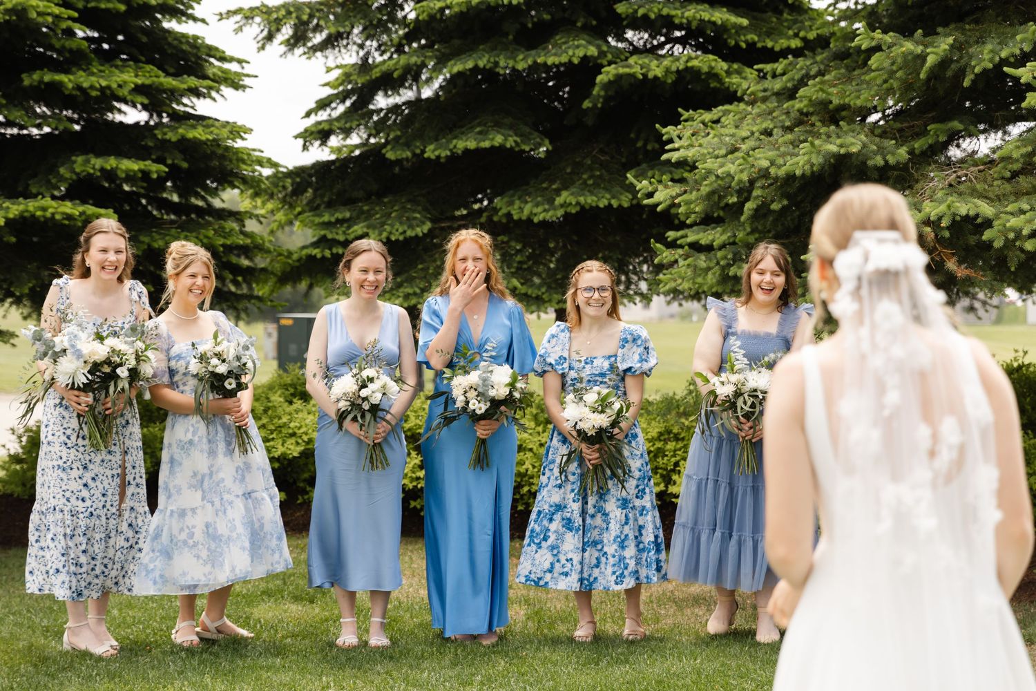 Wedding party in coordinated blue and floral dresses posing outdoors for group photos.