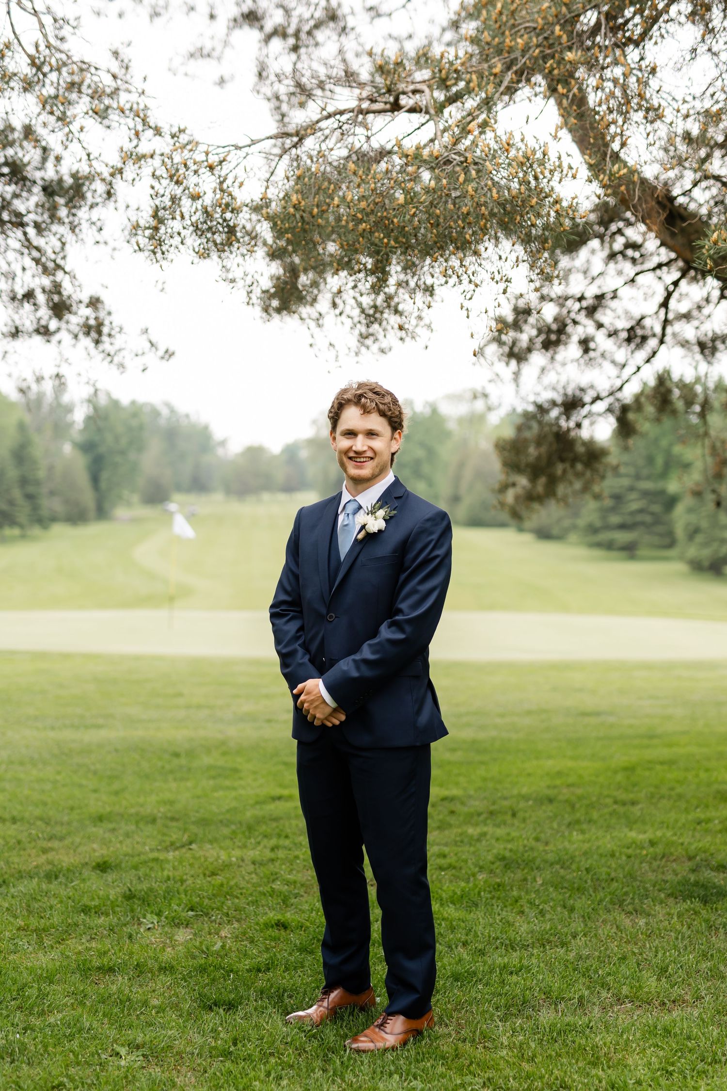 Wedding attire featuring navy suit and boutonniere against a scenic golf course background.