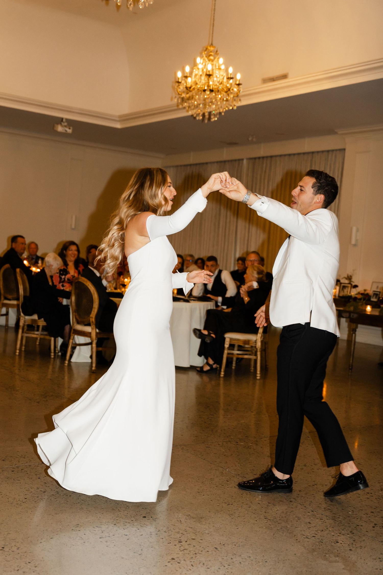Newlyweds performing a lively dance routine in a ballroom with guests watching.