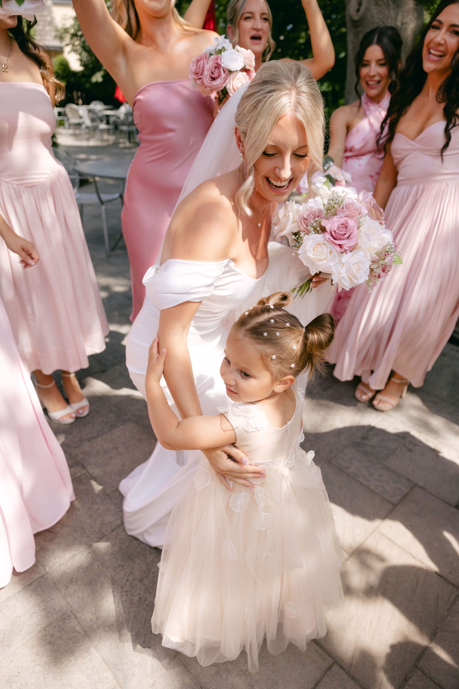 Wedding party in pink dresses and white gowns share joyful moments in outdoor garden setting.