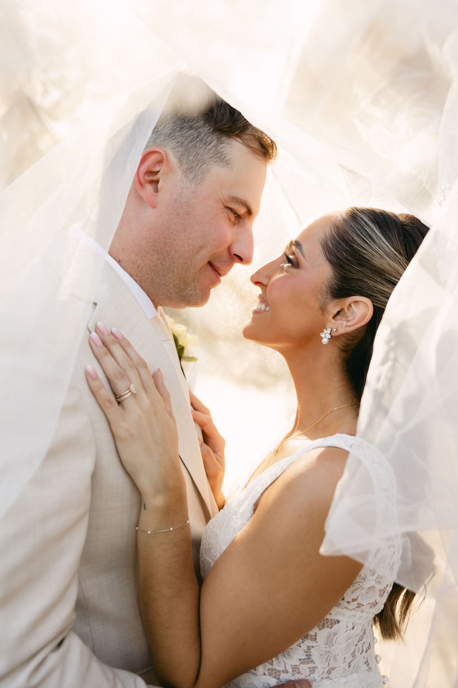 Tender moment between newlyweds as they embrace under a flowing veil.