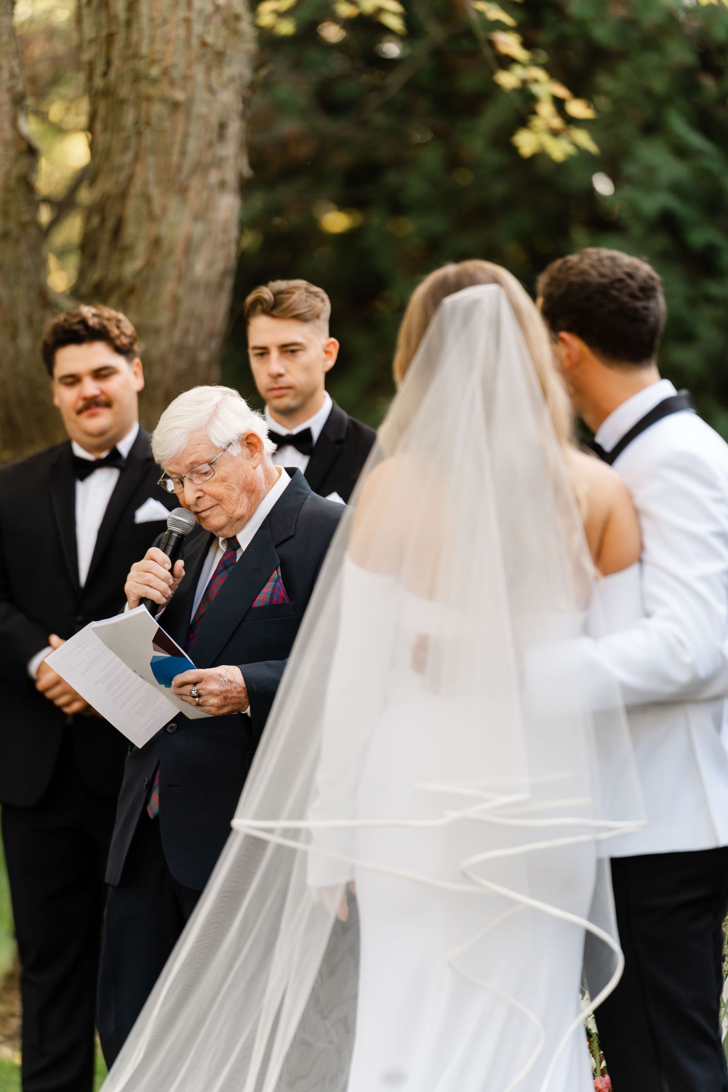 Outdoor wedding ceremony with guests seated on white chairs as vows are exchanged.