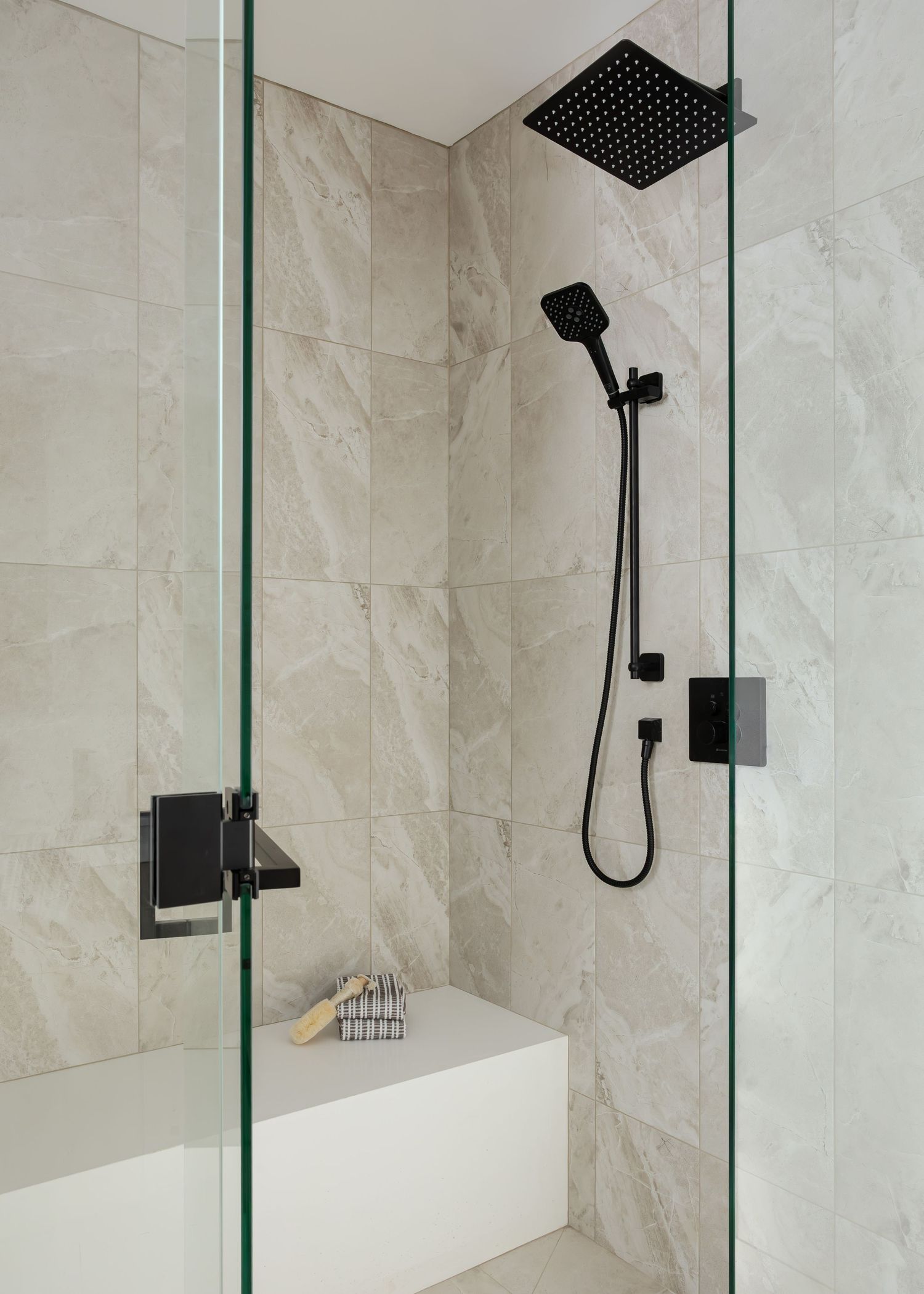 Luxurious marble-tiled shower with black fixtures and glass enclosure offers a spa-like experience.