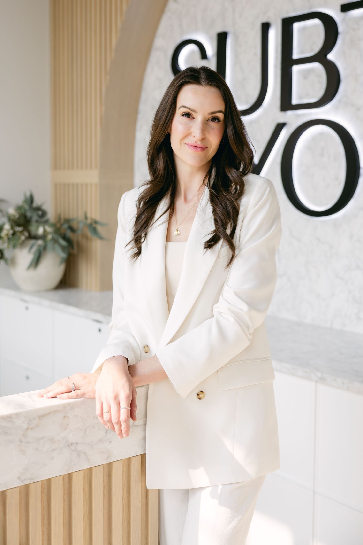 Professional portrait series showing someone in a crisp white blazer seated against a modern beige and white interior.