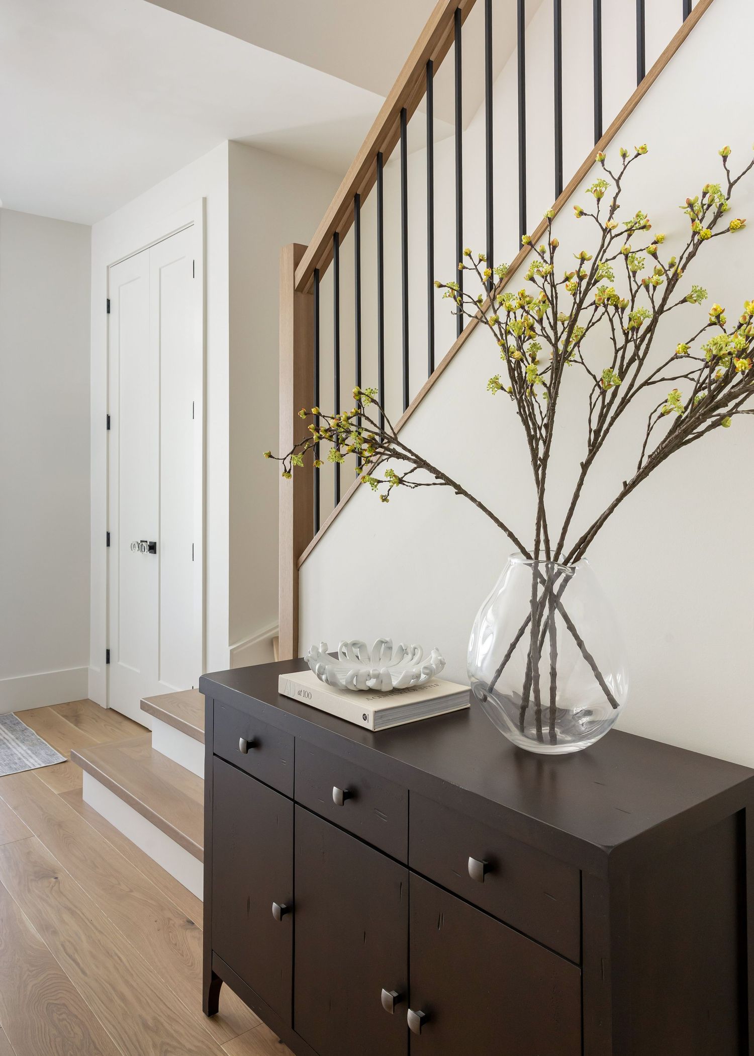 Modern black console table with decorative branches in a glass vase against a white wall with wooden flooring.