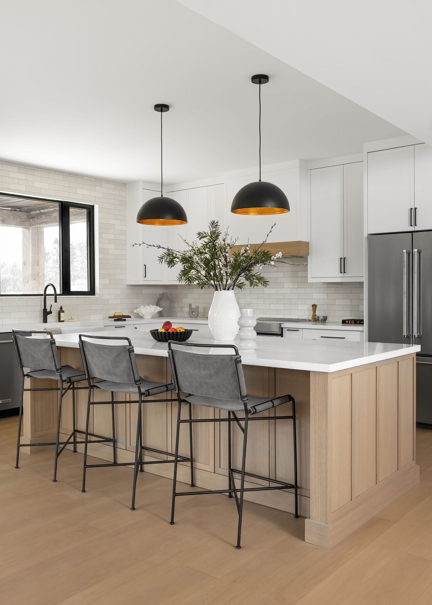 Modern kitchen with white marble island, light wood cabinets, black dome pendant lights and gray bar stools.
