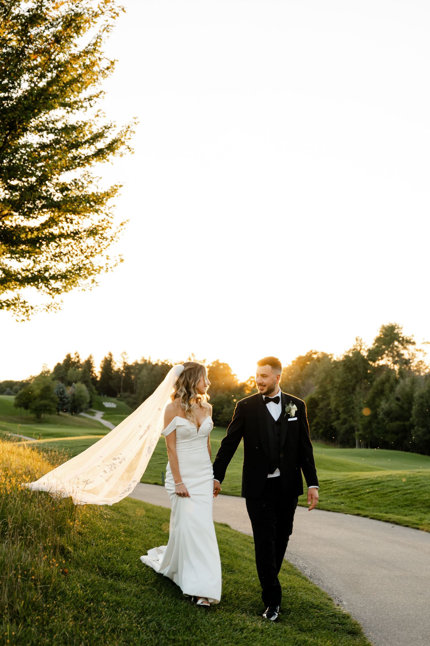 Wedding couple strolls along a curved path with a long flowing veil in the golden evening light.