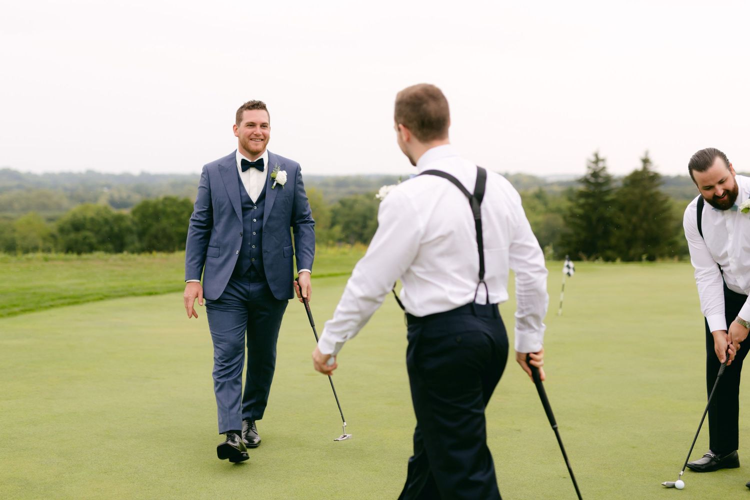 Wedding party members practicing their golf putts on a scenic course green.