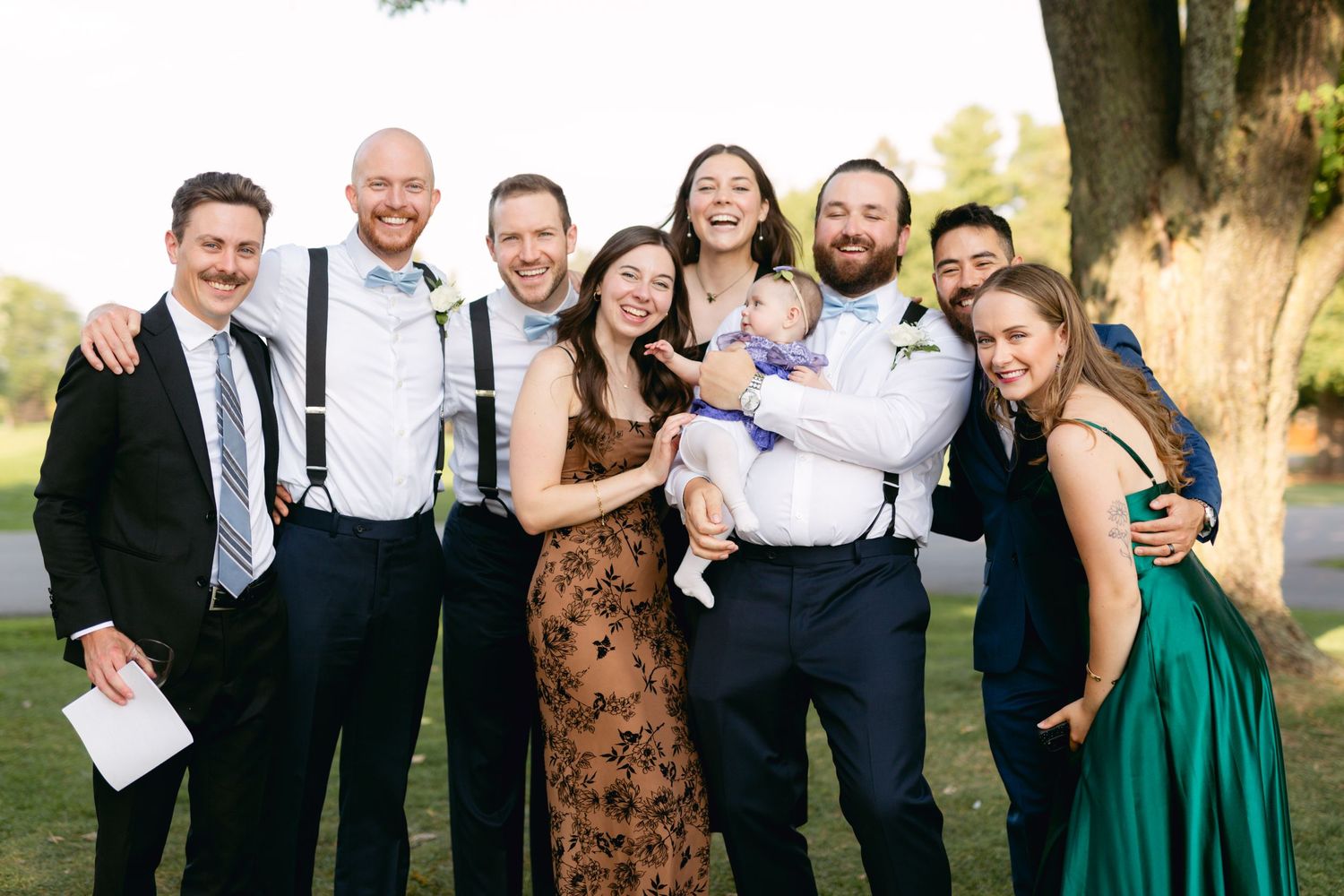Wedding party group poses together outdoors in formal attire.