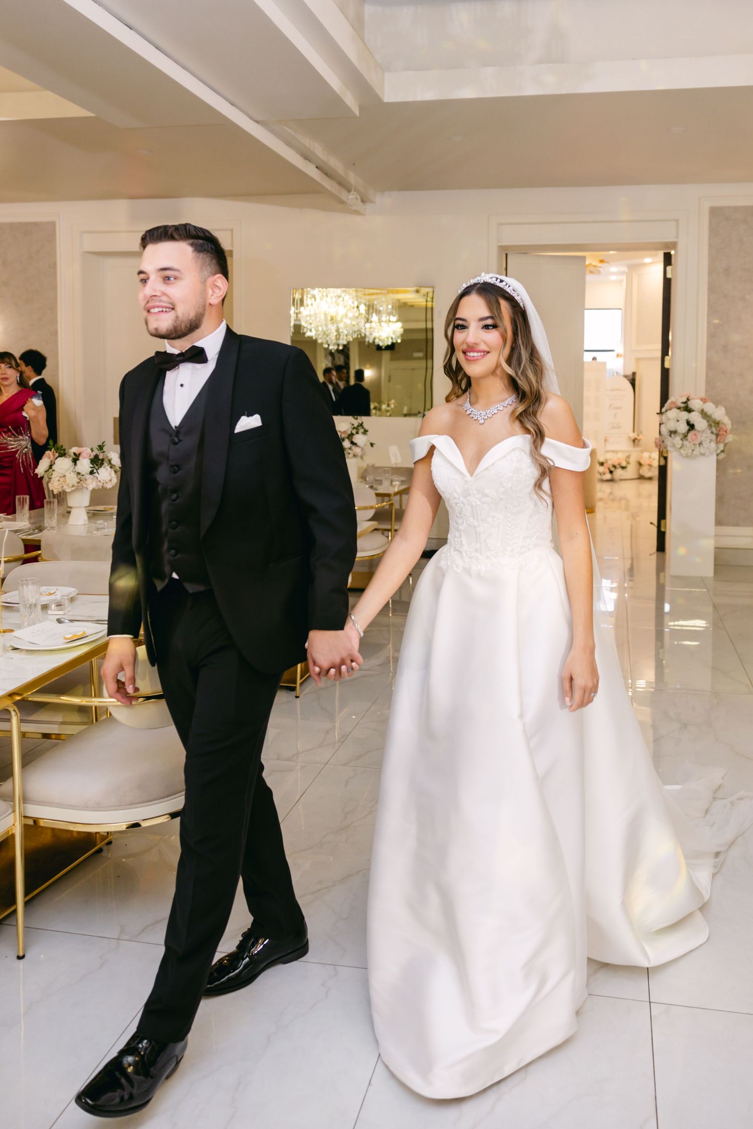 Newlyweds walking hand in hand through an elegant white reception venue.