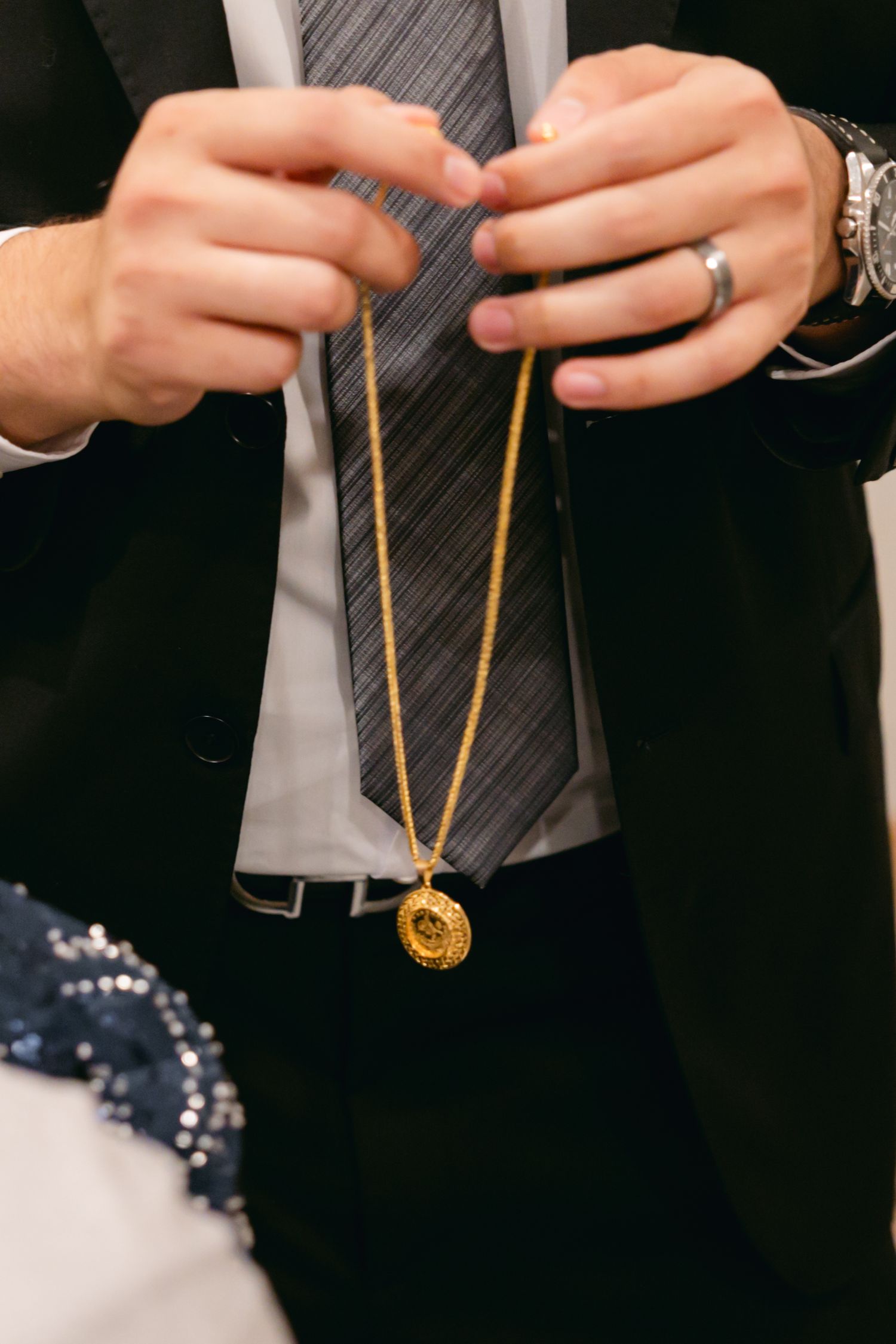 Hands holding a gold necklace against a dark formal suit.
