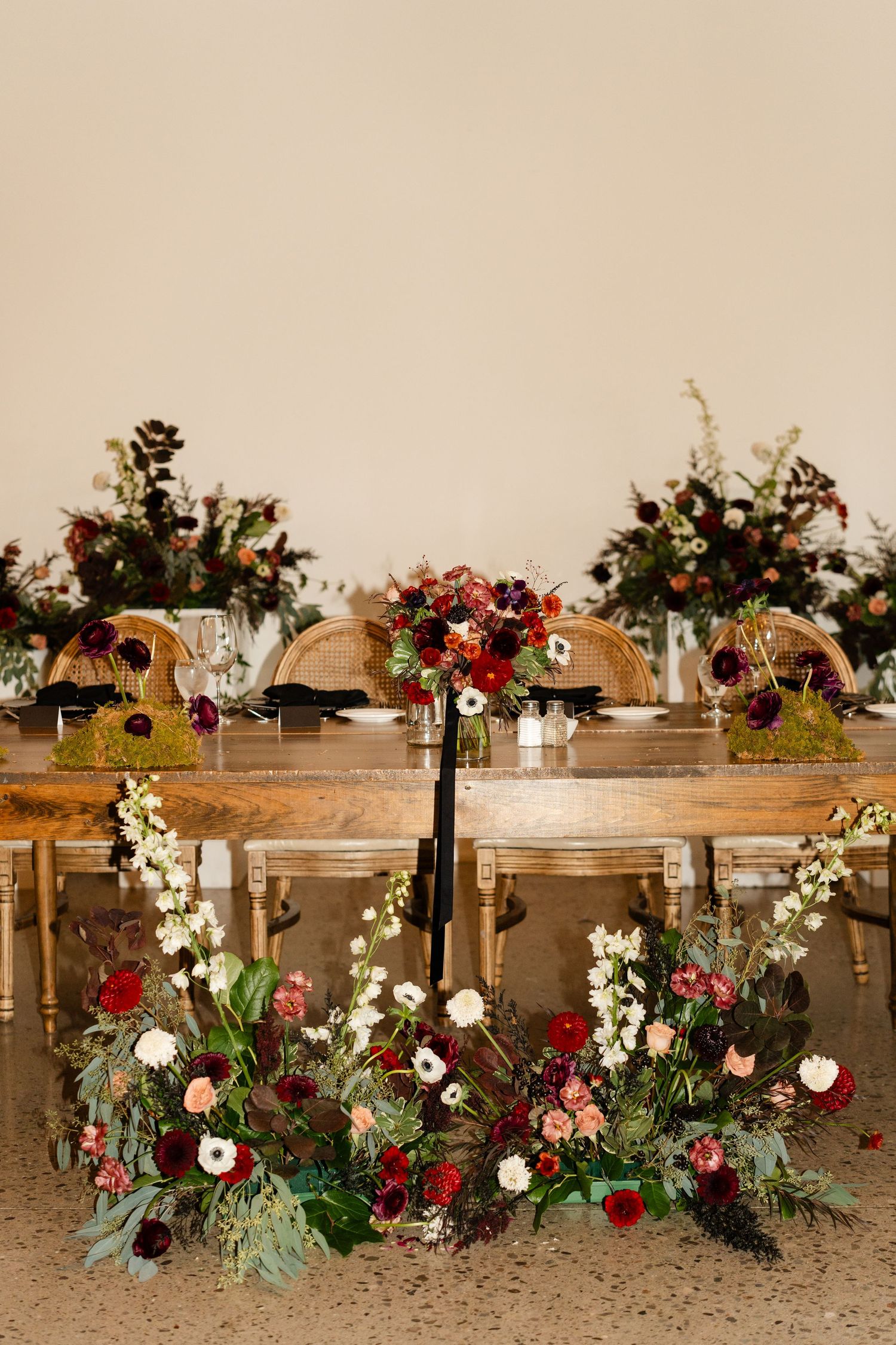Rustic wooden table decorated with lush floral arrangements in red and white.