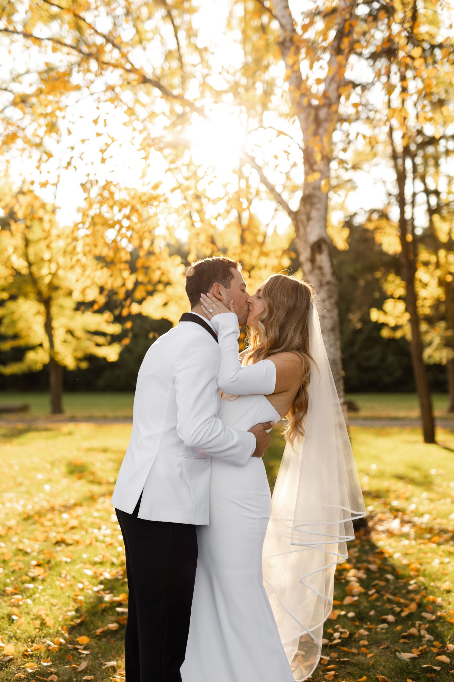 Newlyweds share intimate moments in a sunlit autumn garden setting.