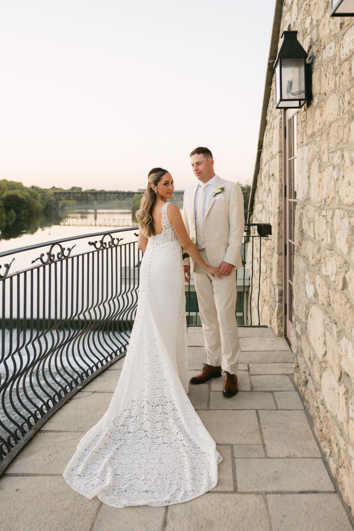 Wedding couple shares romantic moments along stone balcony overlooking water.