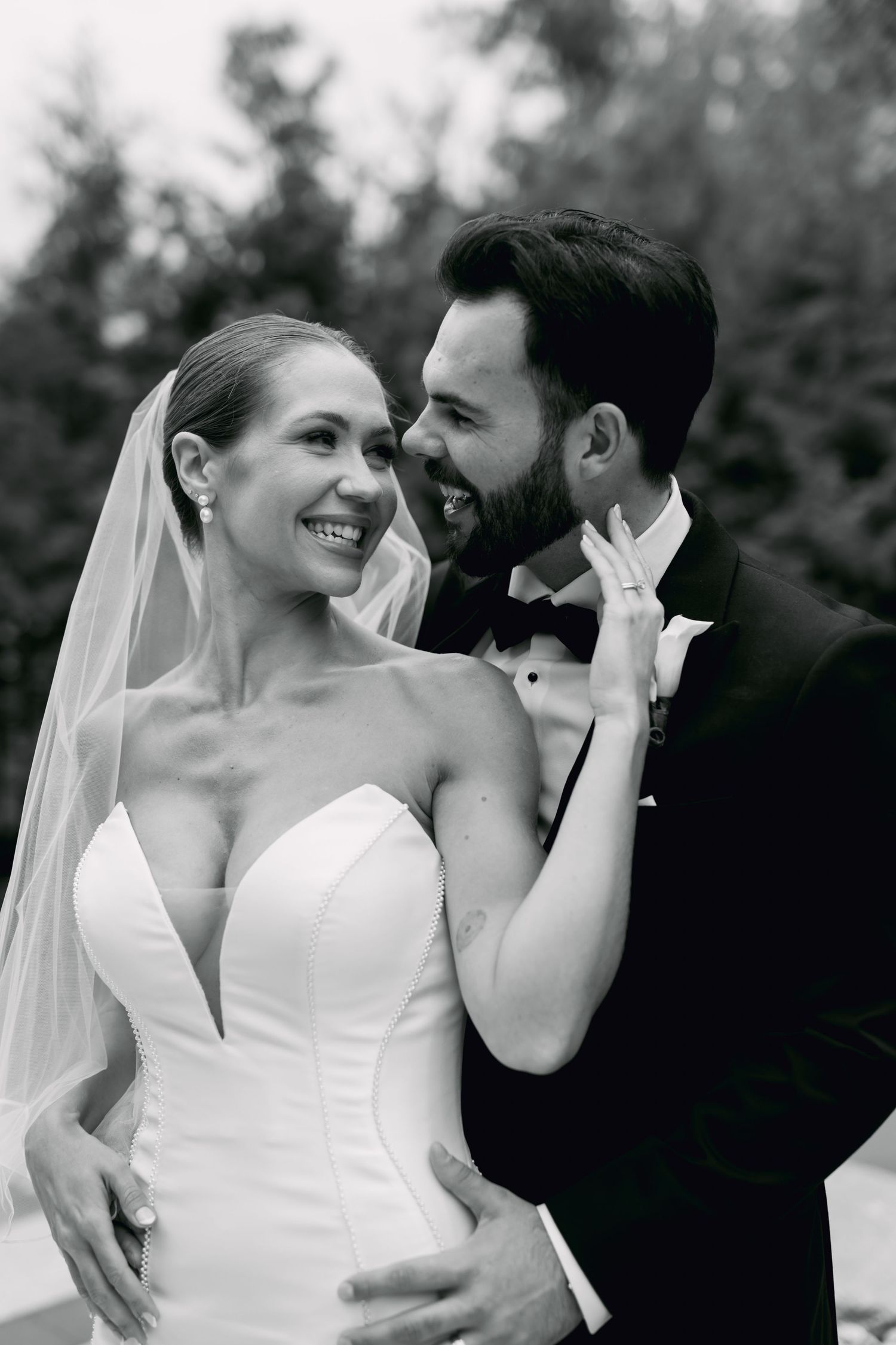 Black and white photo of laughing bride and groom embracing outdoors after wedding ceremony.