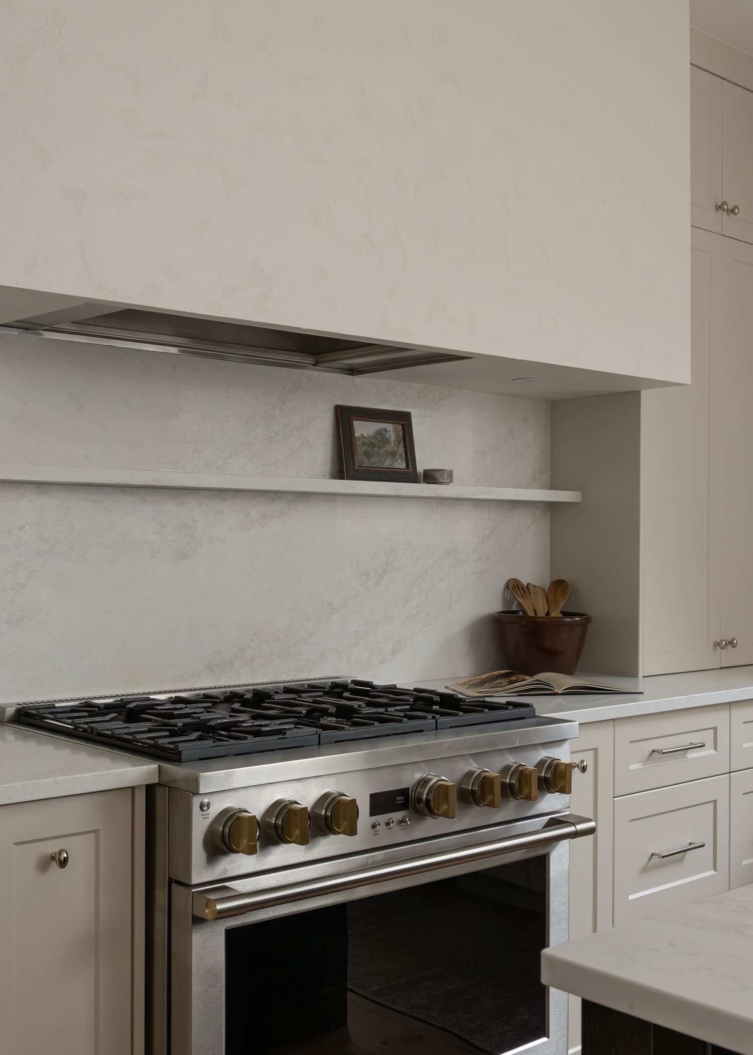 Professional-grade gas range with stainless steel hood vent in white kitchen cabinetry.