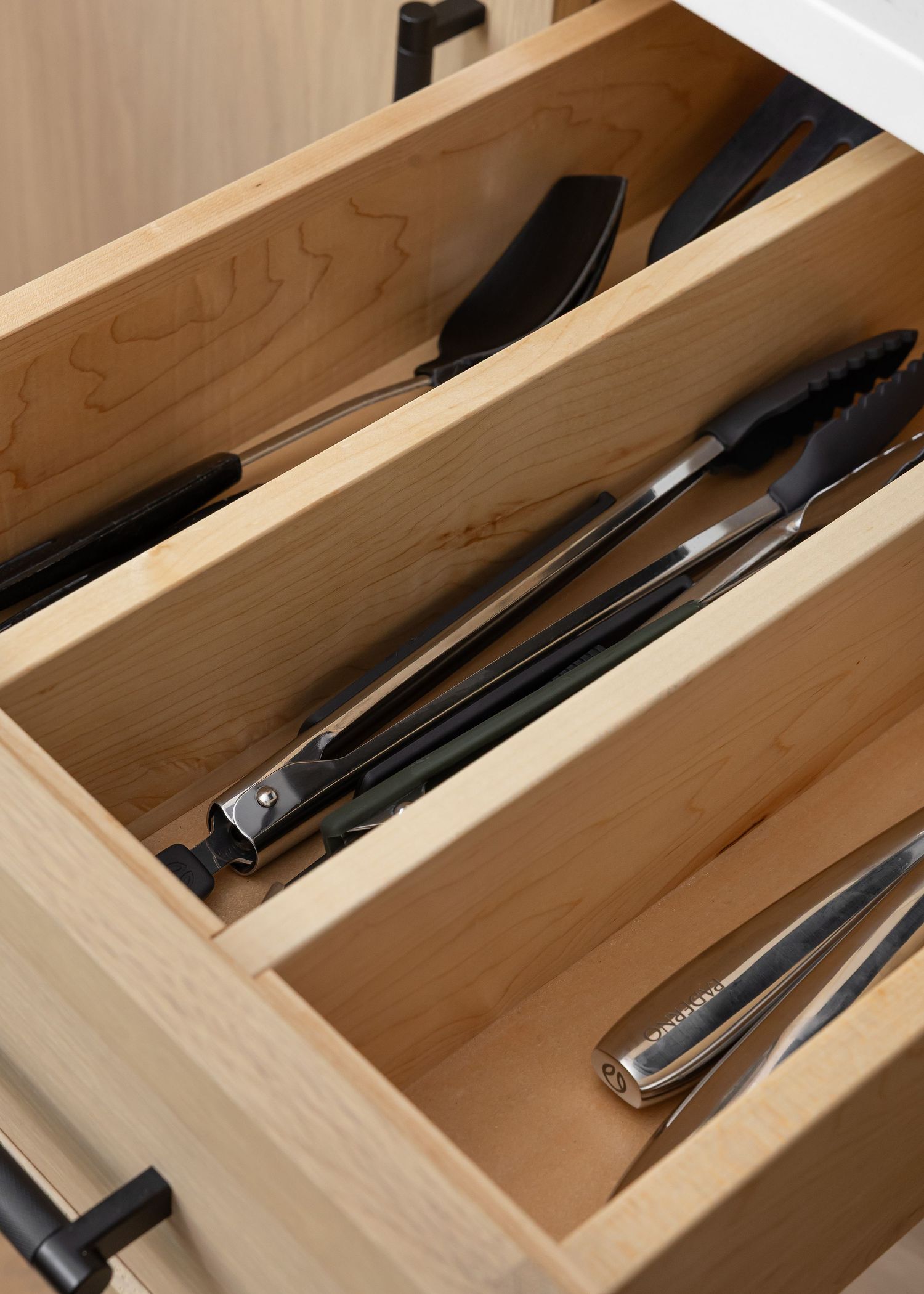 Wooden kitchen drawer organizer with black utensils and cooking tools neatly arranged in compartments.