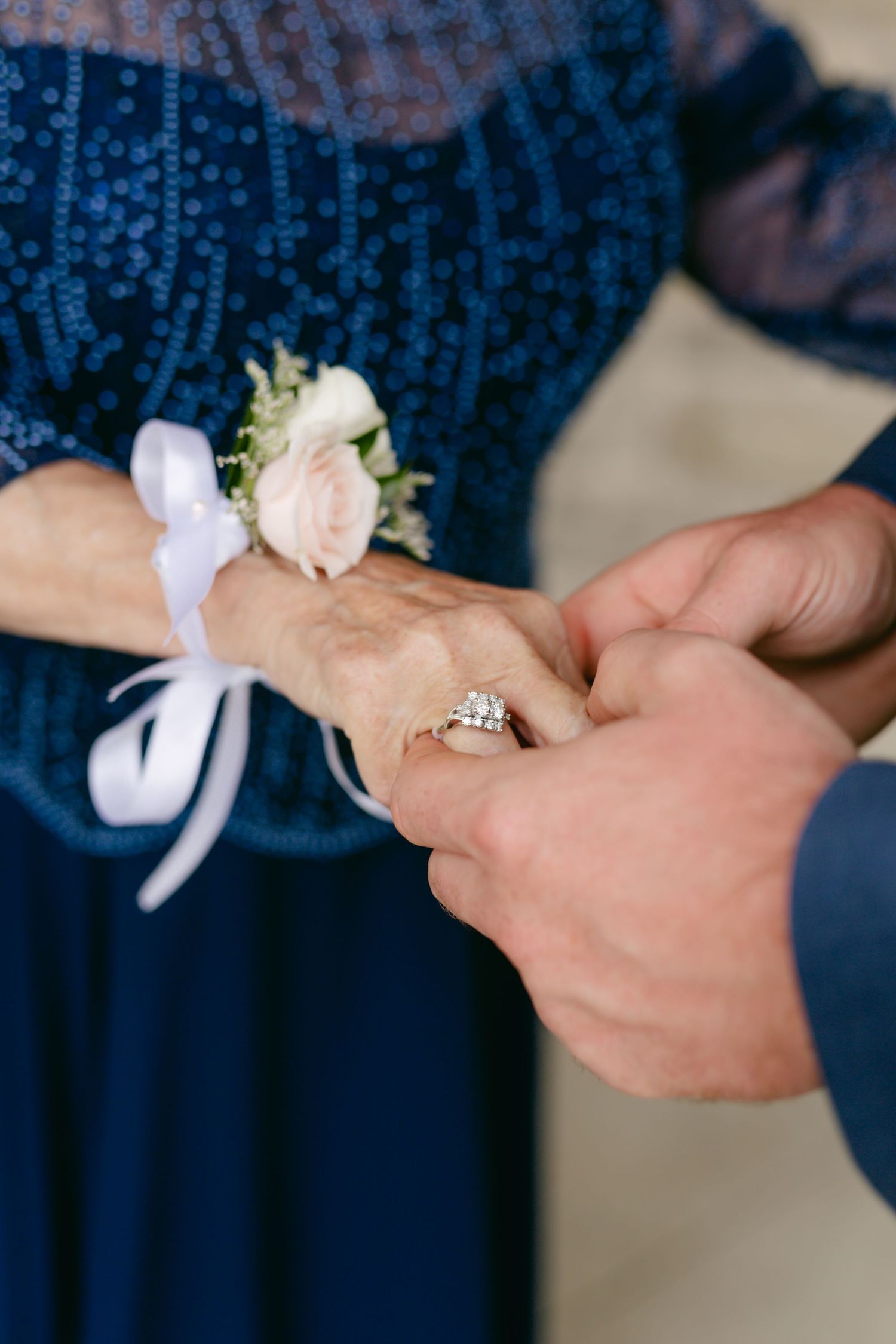 Close-up of hands placing a delicate white corsage with ribbon on a navy blue lace dress.