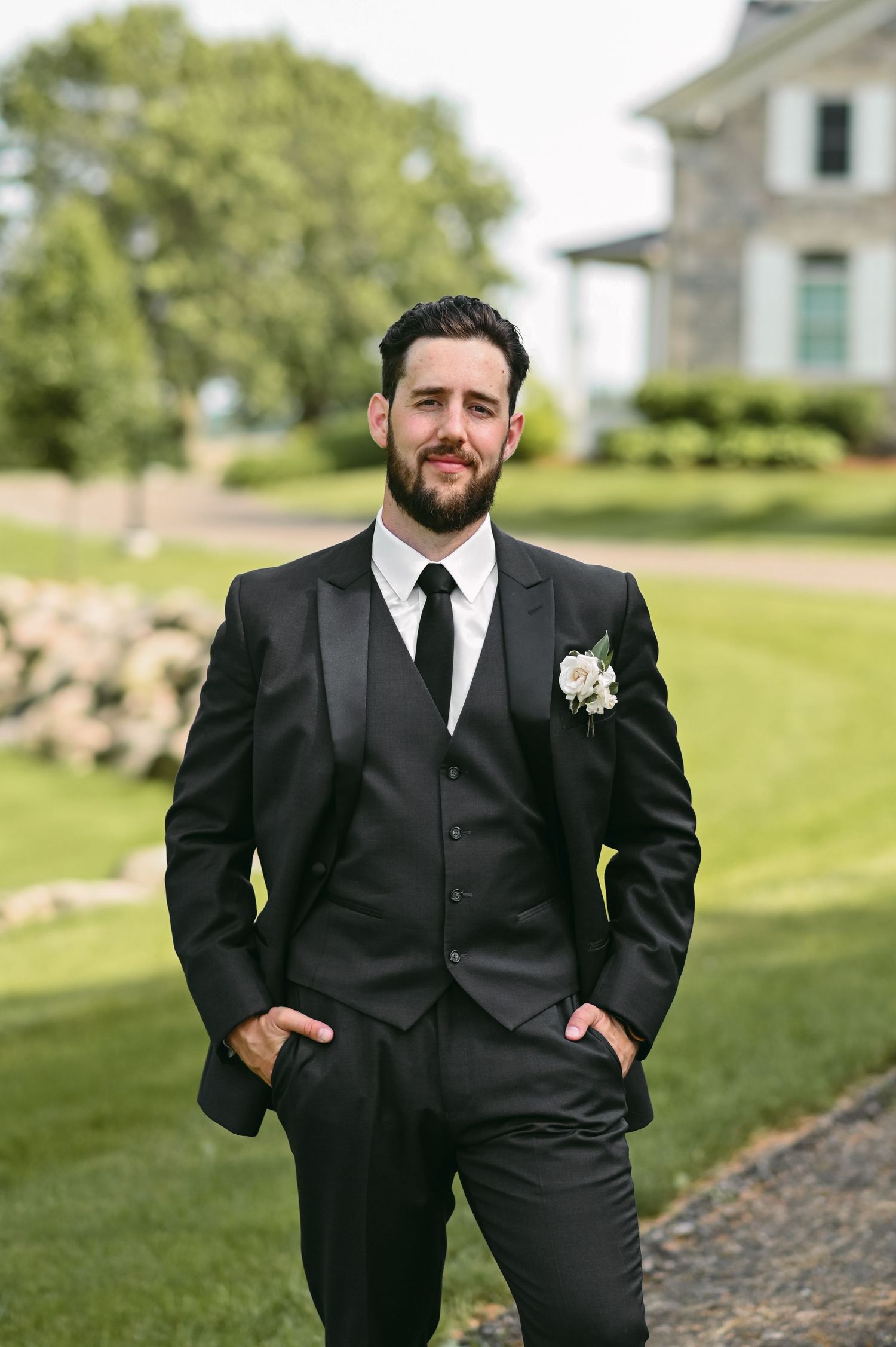 Groomsmen in classic black tuxedos pose for portraits on a green lawn.