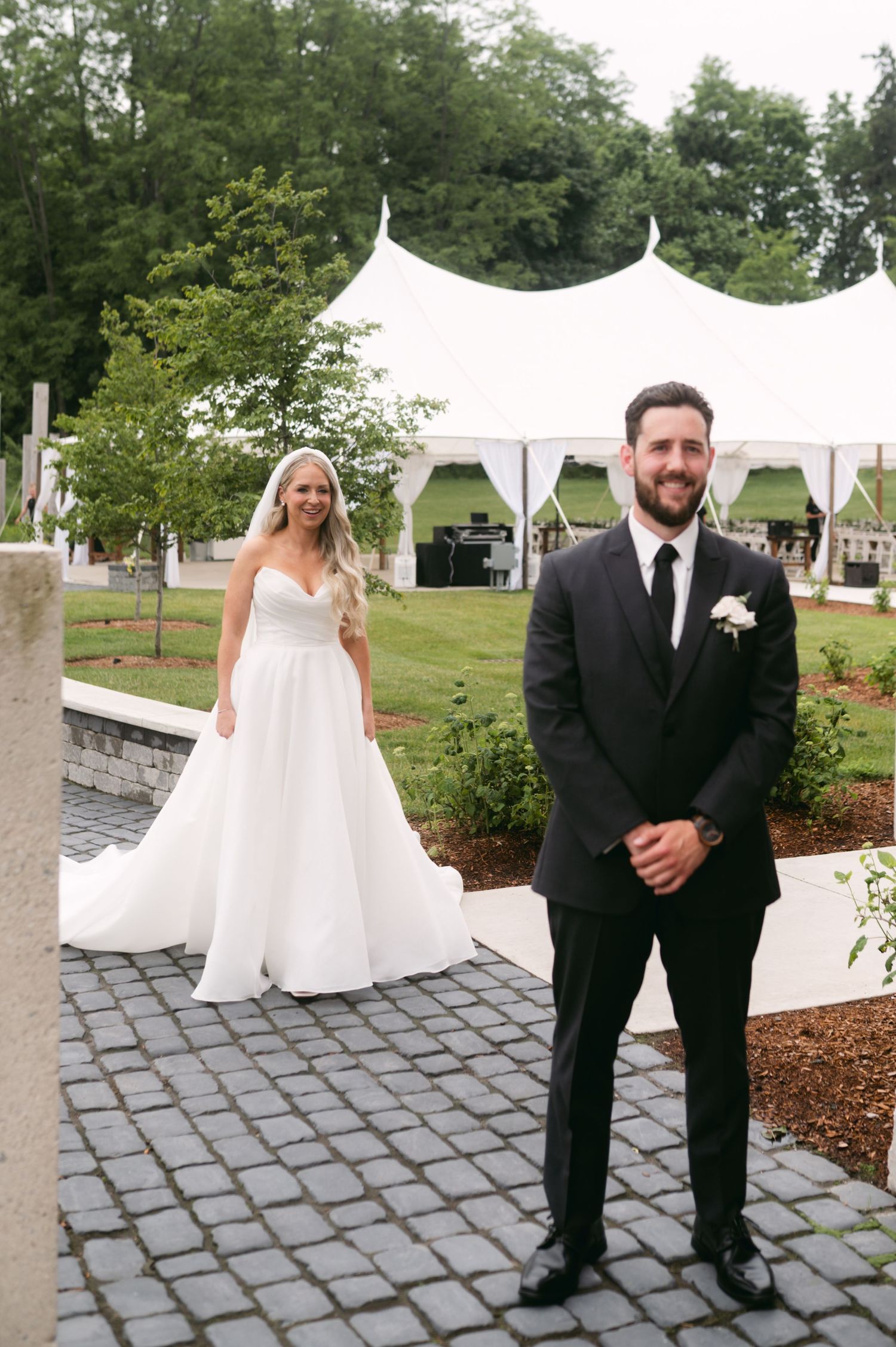 Outdoor wedding setup with couple standing on cobblestone path near white tent.