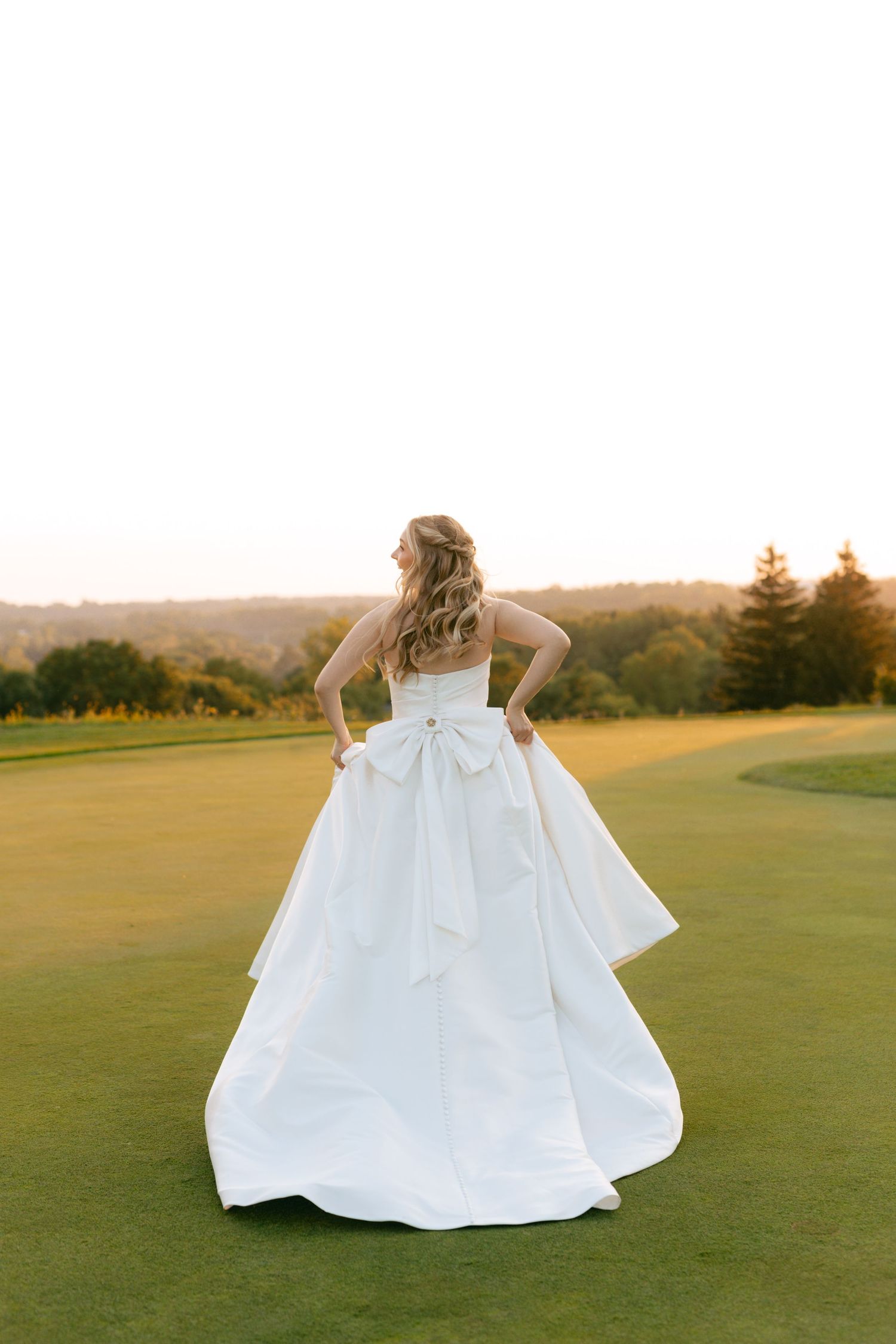 A flowing white wedding dress twirls gracefully across a lush green golf course at sunset.