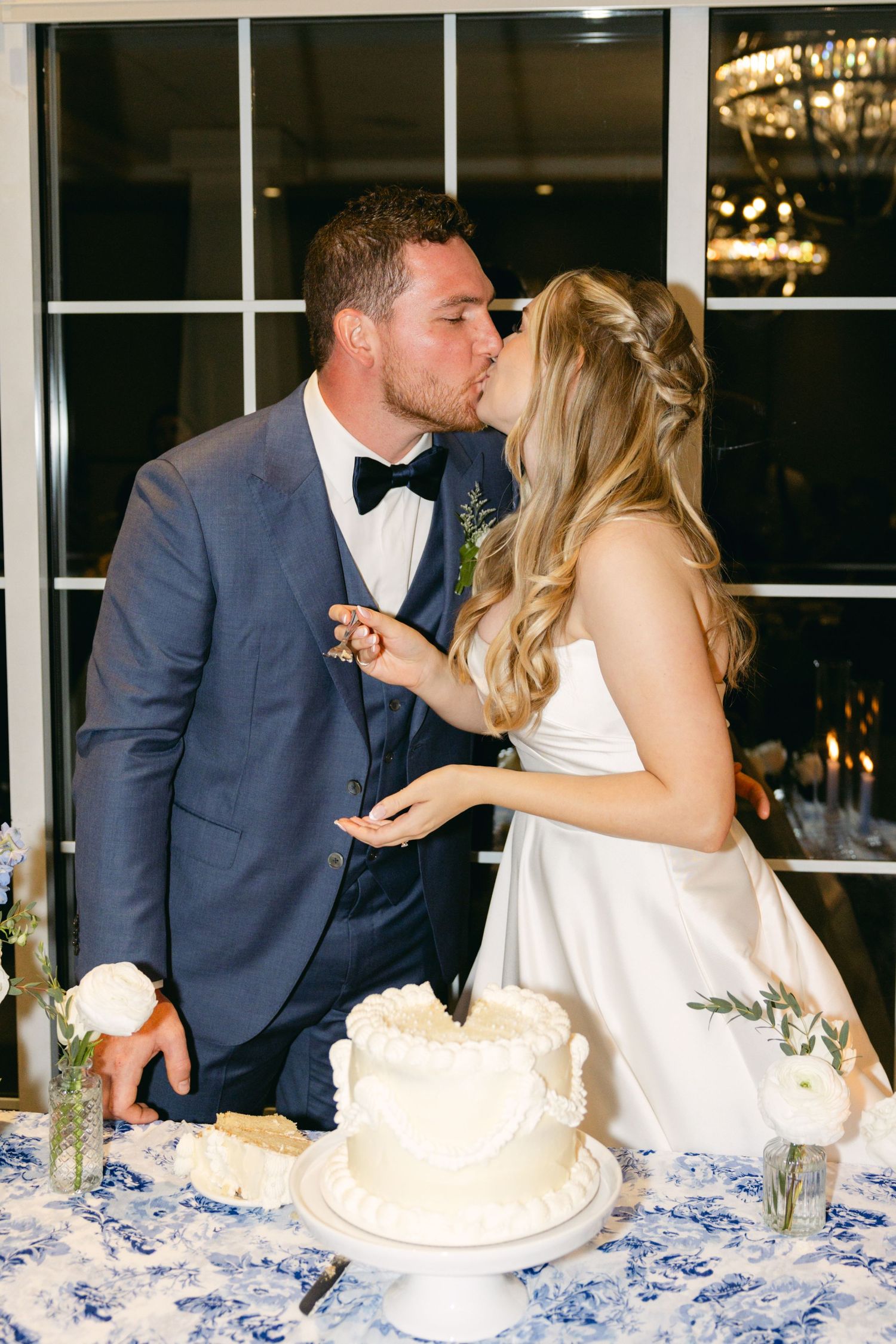 A romantic moment as newlyweds share a kiss while cutting their wedding cake.