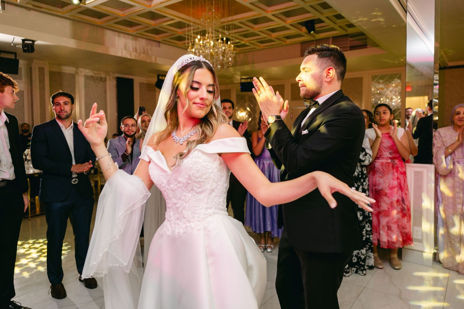 A couple shares their first dance as newlyweds in an elegant ballroom with crystal chandeliers.