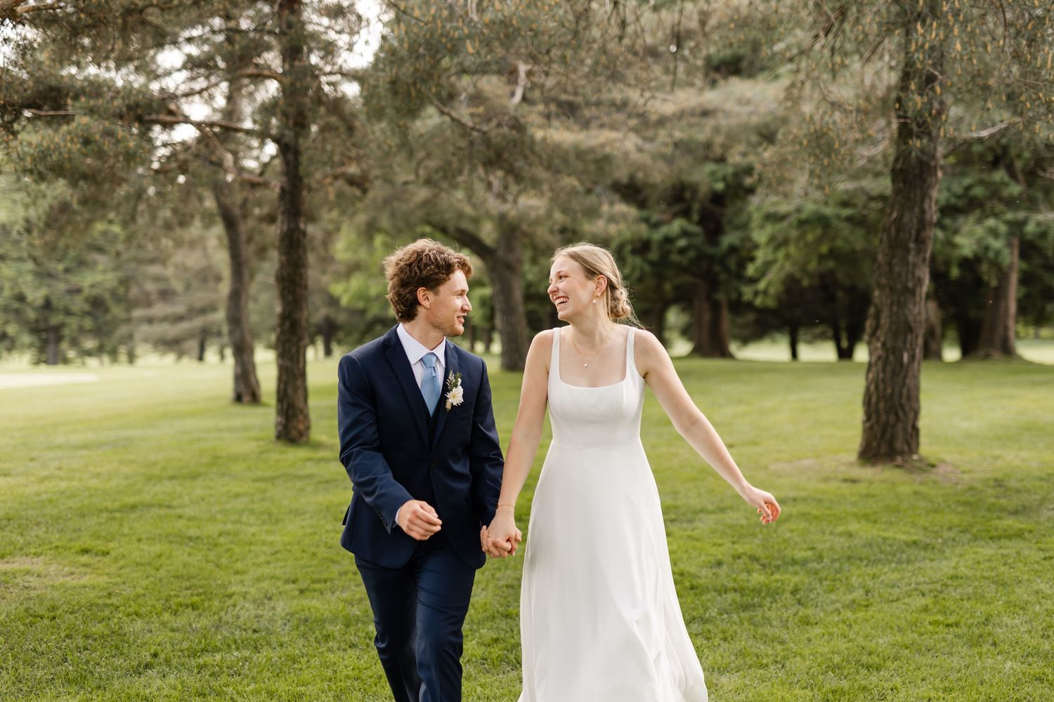 Newlyweds share a playful moment while walking through a scenic park setting.