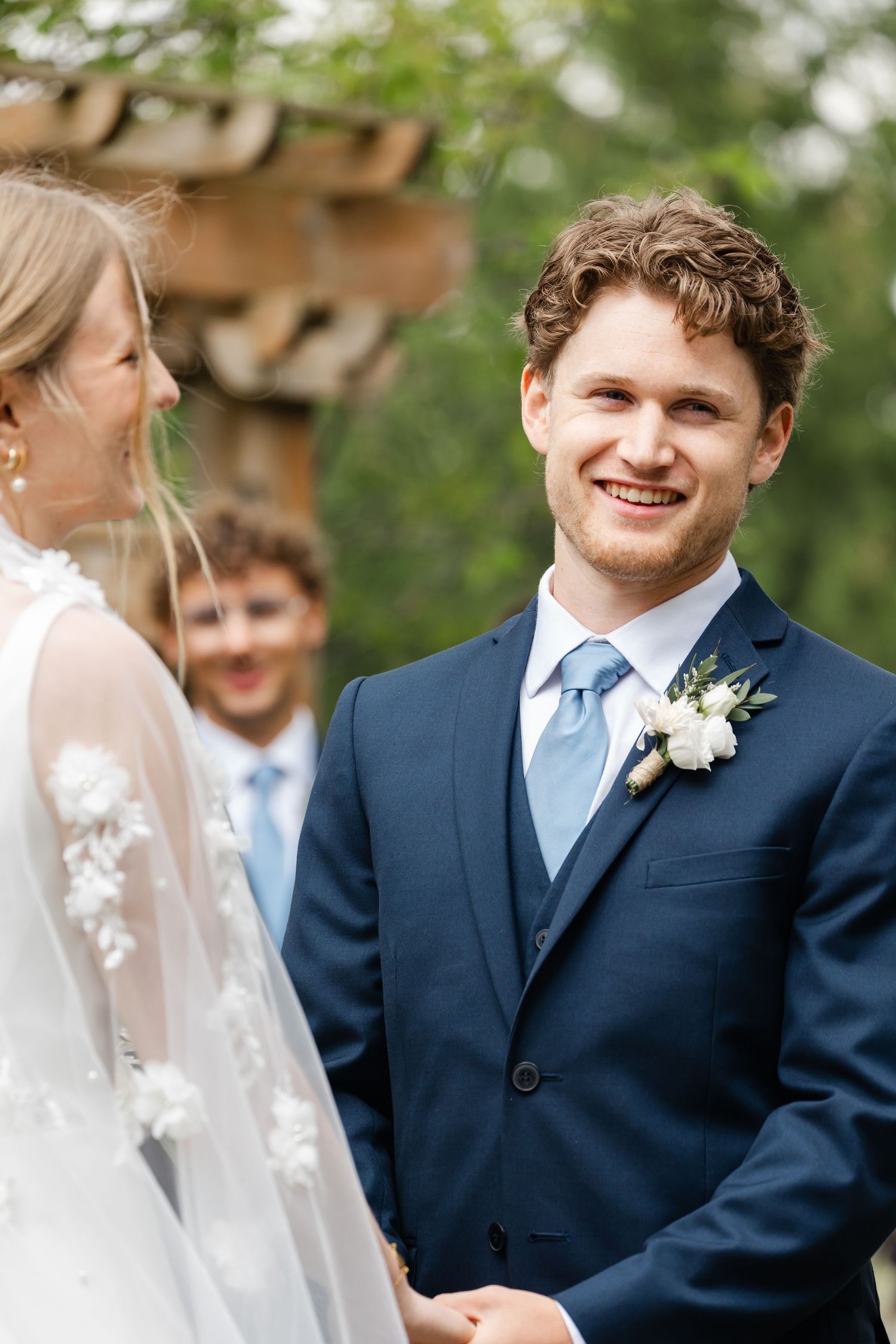 Outdoor wedding ceremony with couple exchanging vows in front of wooden arbor.