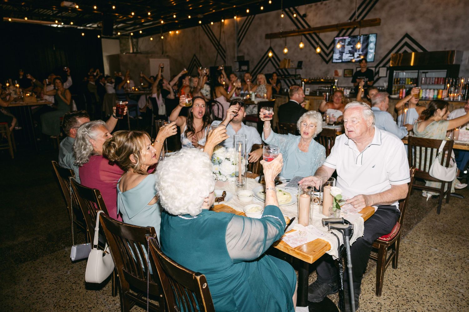 Wedding reception venue filled with guests seated at tables under ambient lighting.