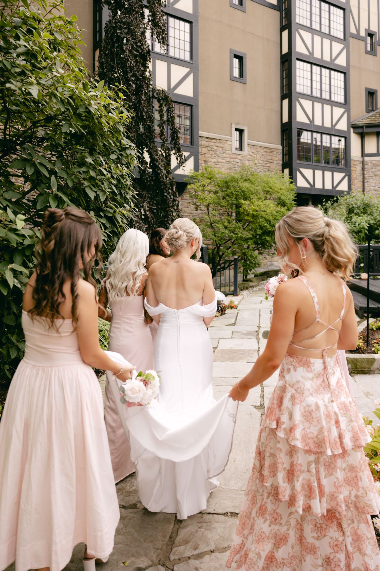 Bridesmaids in pink and white dresses walking down stone steps at an outdoor venue.