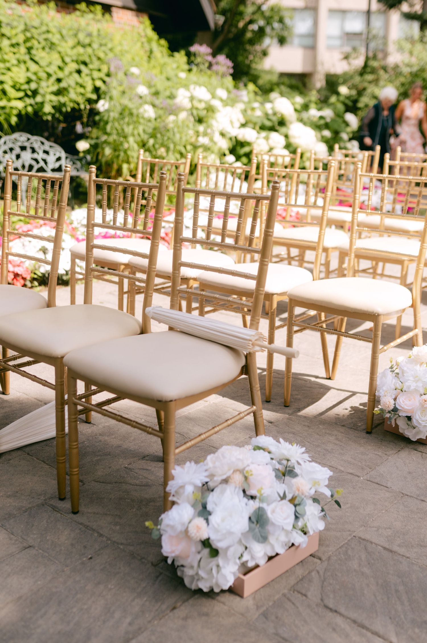 Gold chiavari chairs lined up for an outdoor wedding ceremony with white floral arrangements.