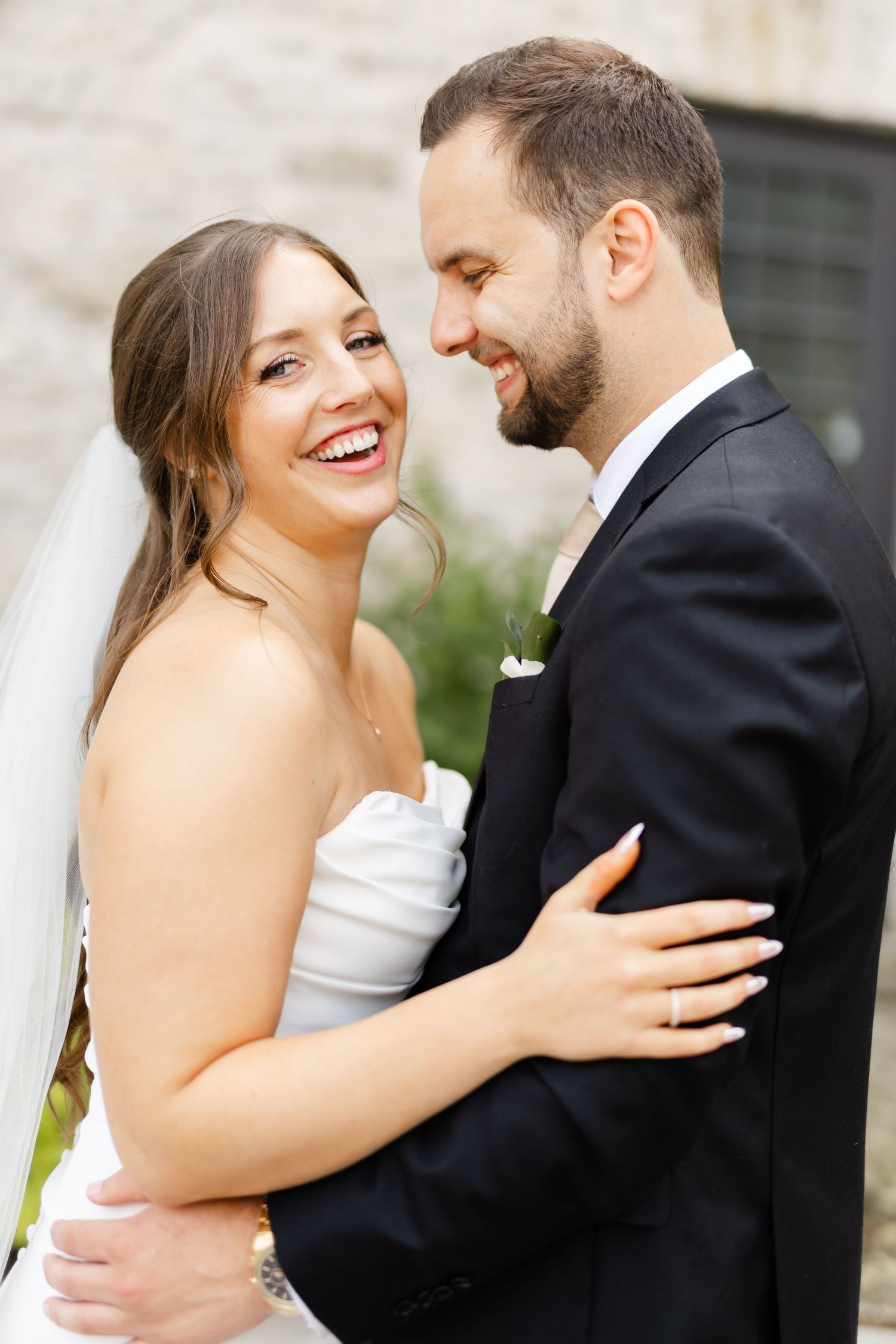 Joyful bride in strapless white gown embracing bearded groom in black suit during outdoor wedding portraits.