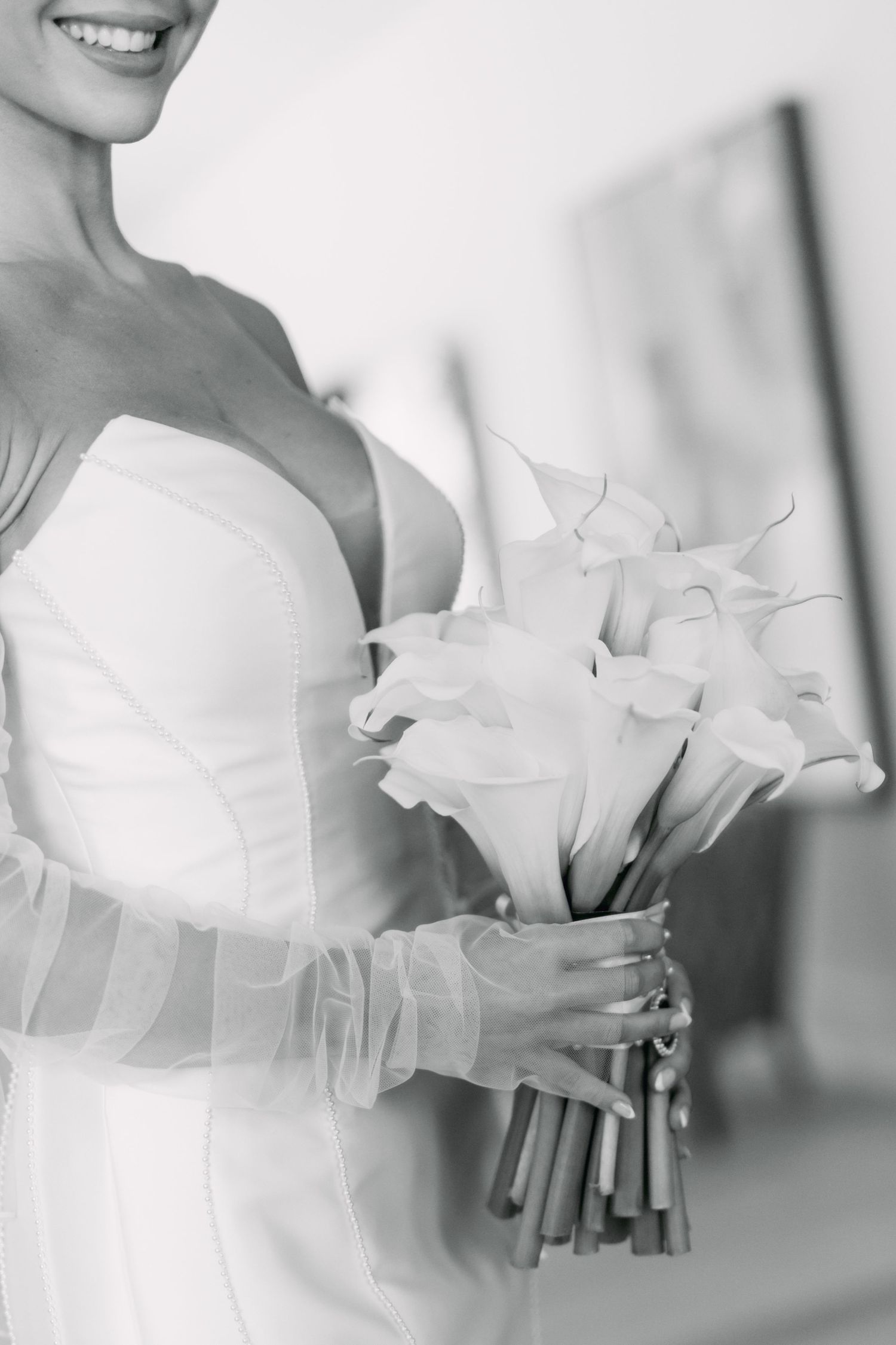 Black and white photo of bride in strapless gown holding beautiful calla lily wedding bouquet.